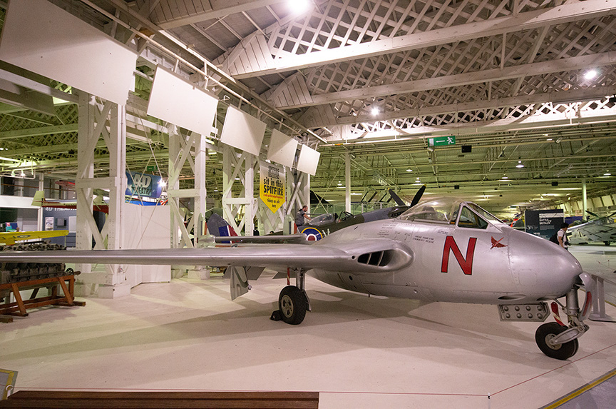 The image shows an aircraft displayed in a museum or exhibition hall. The aircraft has a sleek, silver body with a prominent red 'N' on its side. The setting appears to be indoors with high ceilings and large windows, allowing natural light to illuminate the space. Other aircraft and exhibits are visible in the background, suggesting a dedicated aviation or military history exhibit.
