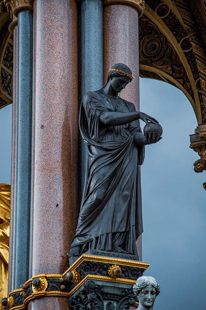 The image depicts a statue of a robed figure holding a celestial globe, standing on a pedestal between two columns. The statue is labeled 'Astronomy' and is part of an ornate architectural structure with intricate gold detailing and decorative elements.