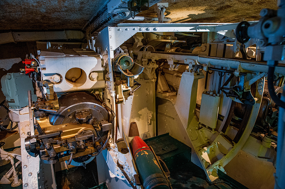 The image shows the interior of a military tank, focusing on the complex machinery and mechanisms involved in operating the main cannon. Various components such as the breech, loading mechanisms, and hydraulic systems are visible, highlighting the intricate engineering involved in tank design. The image provides a detailed view of the mechanical and operational aspects of a tank's main armament system.
