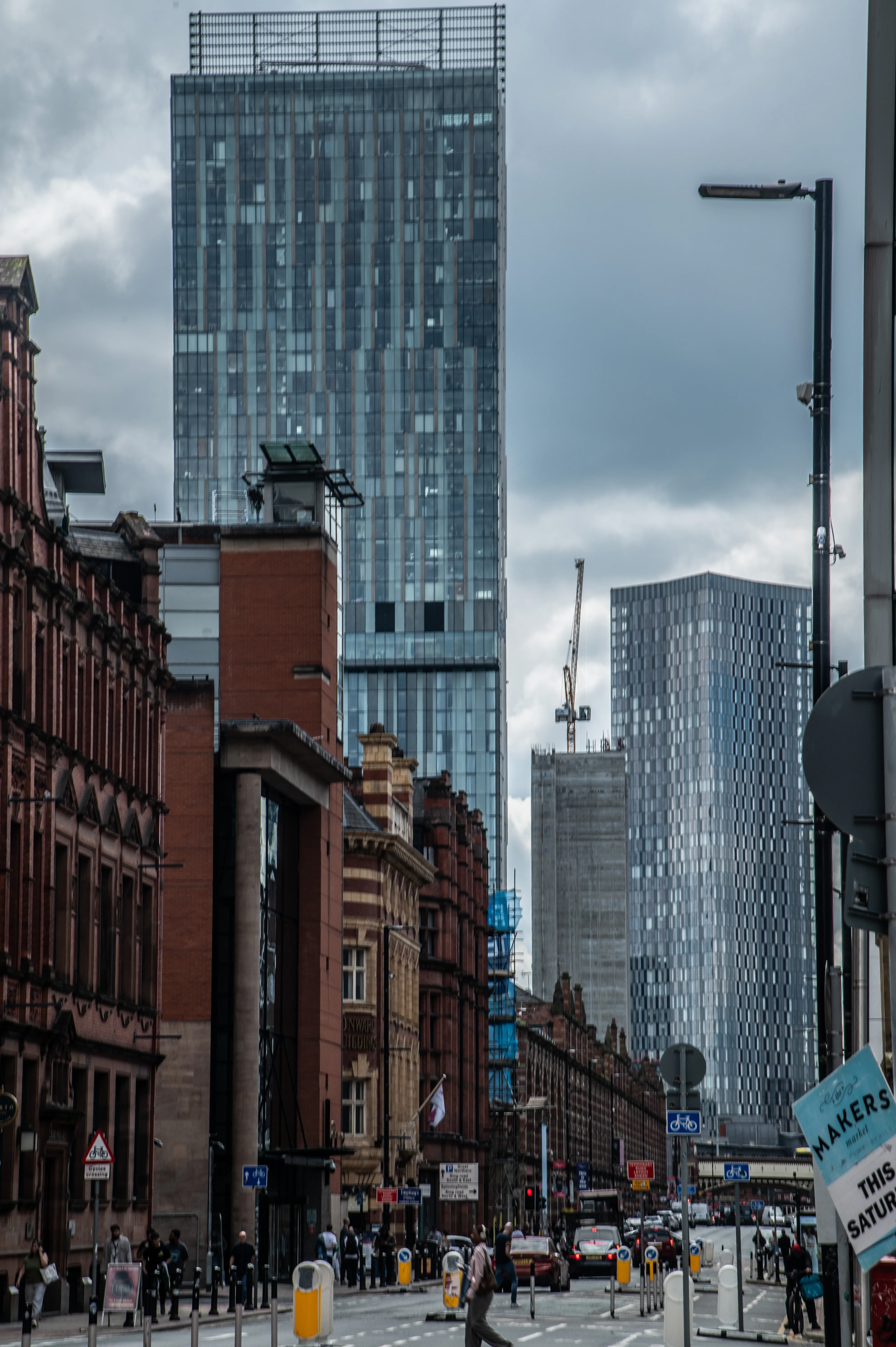 City street with brick buildings, modern glass skyscrapers, pedestrians, cars, and an overcast sky.