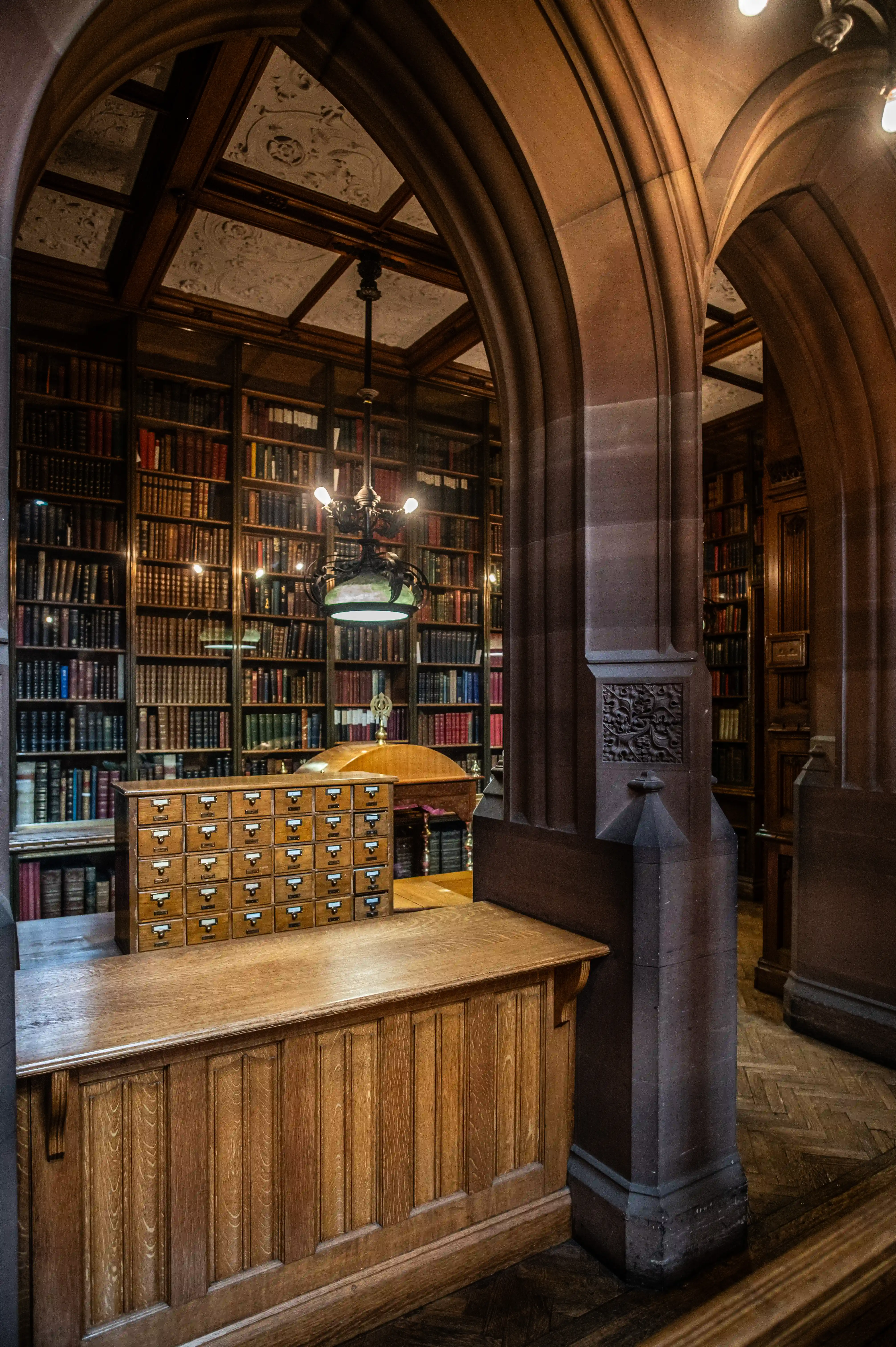 View of a historic library interior with arched columns, tall bookcases and a wooden desk with drawer fronts