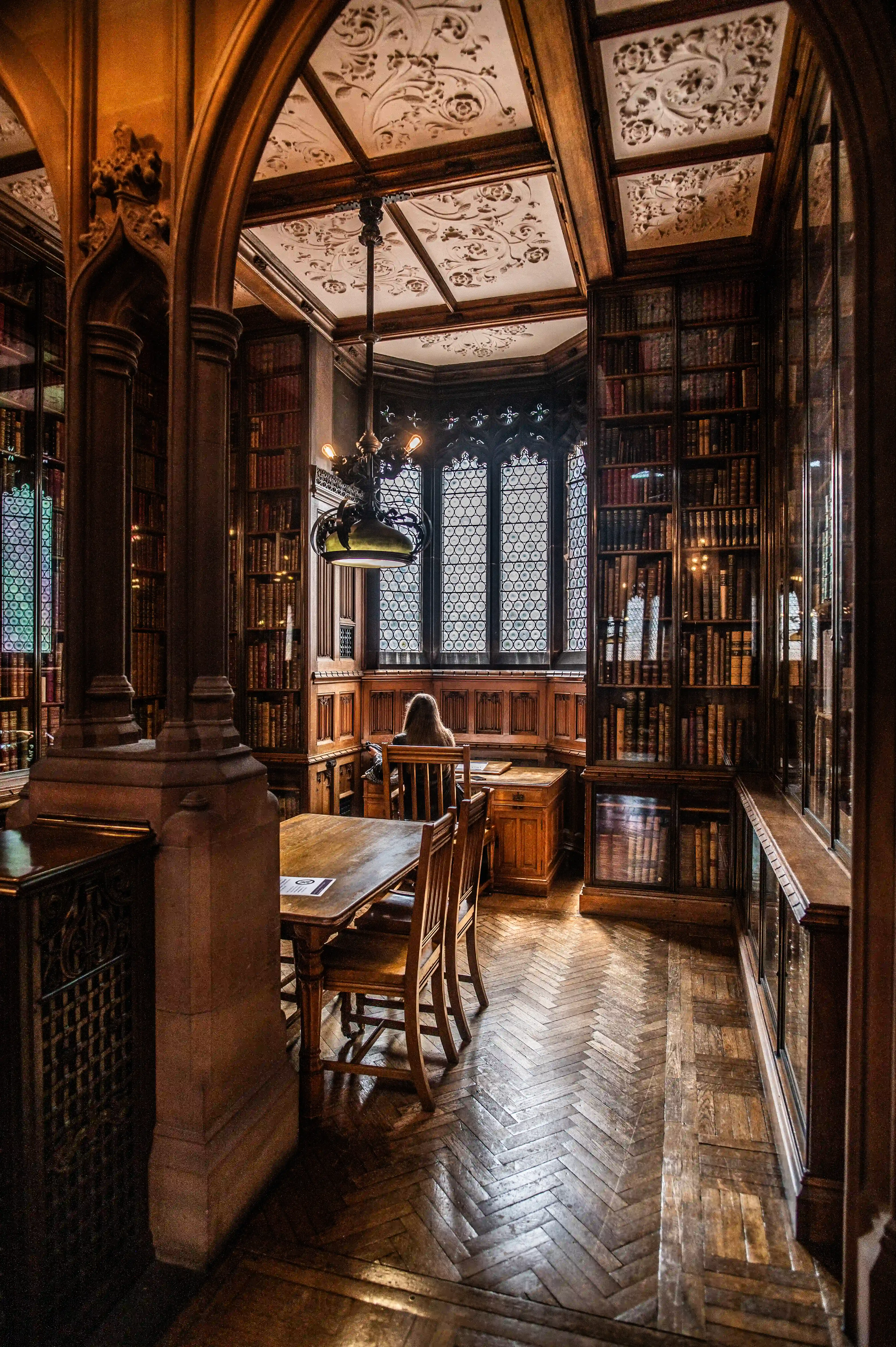 Interior view down a historic library corridor with bookcases, wooden desks and chairs, and an ornate vaulted ceiling