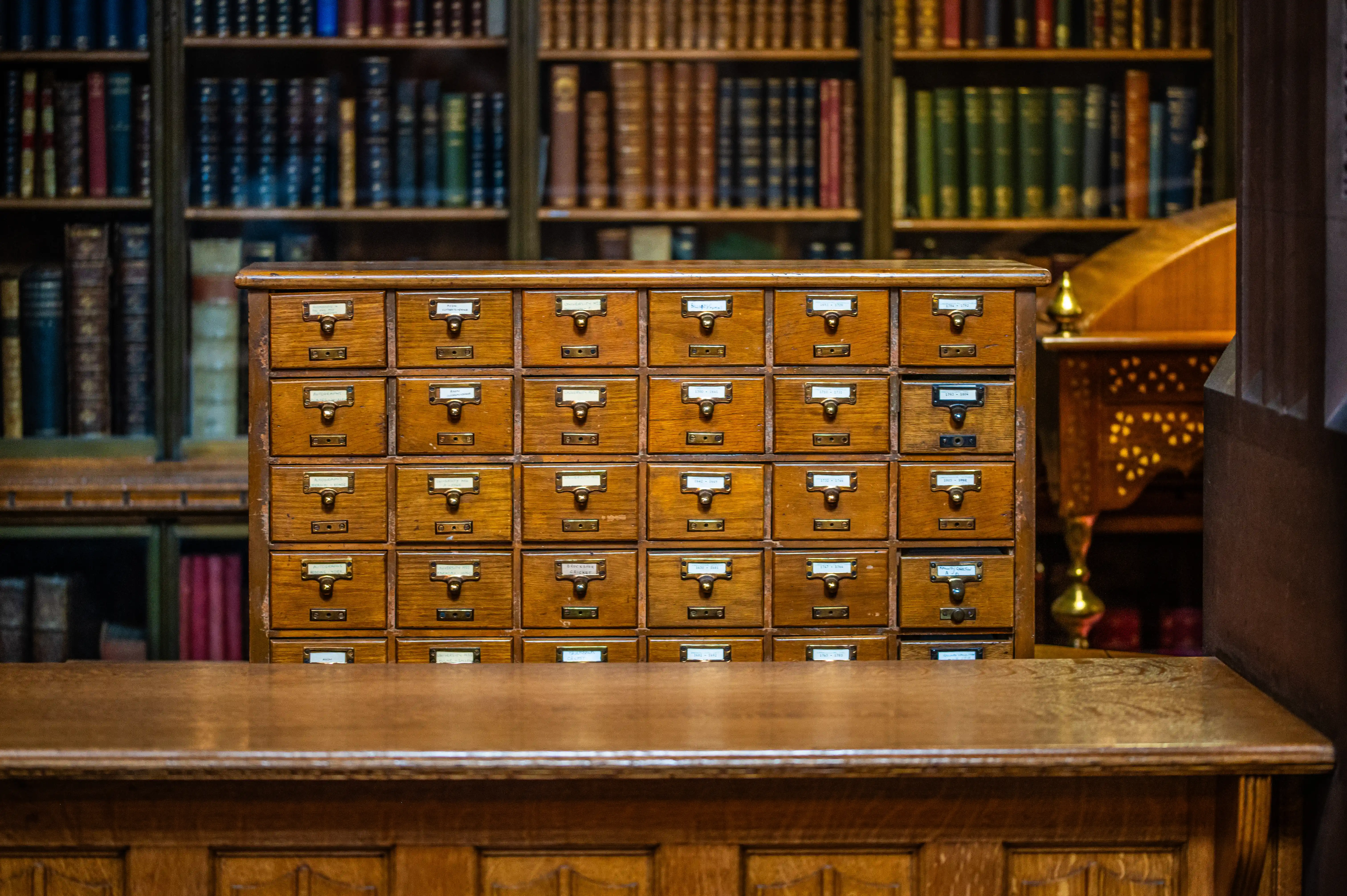 Wooden card catalogue with brass-handled drawers in a historic library, with bookcases behind