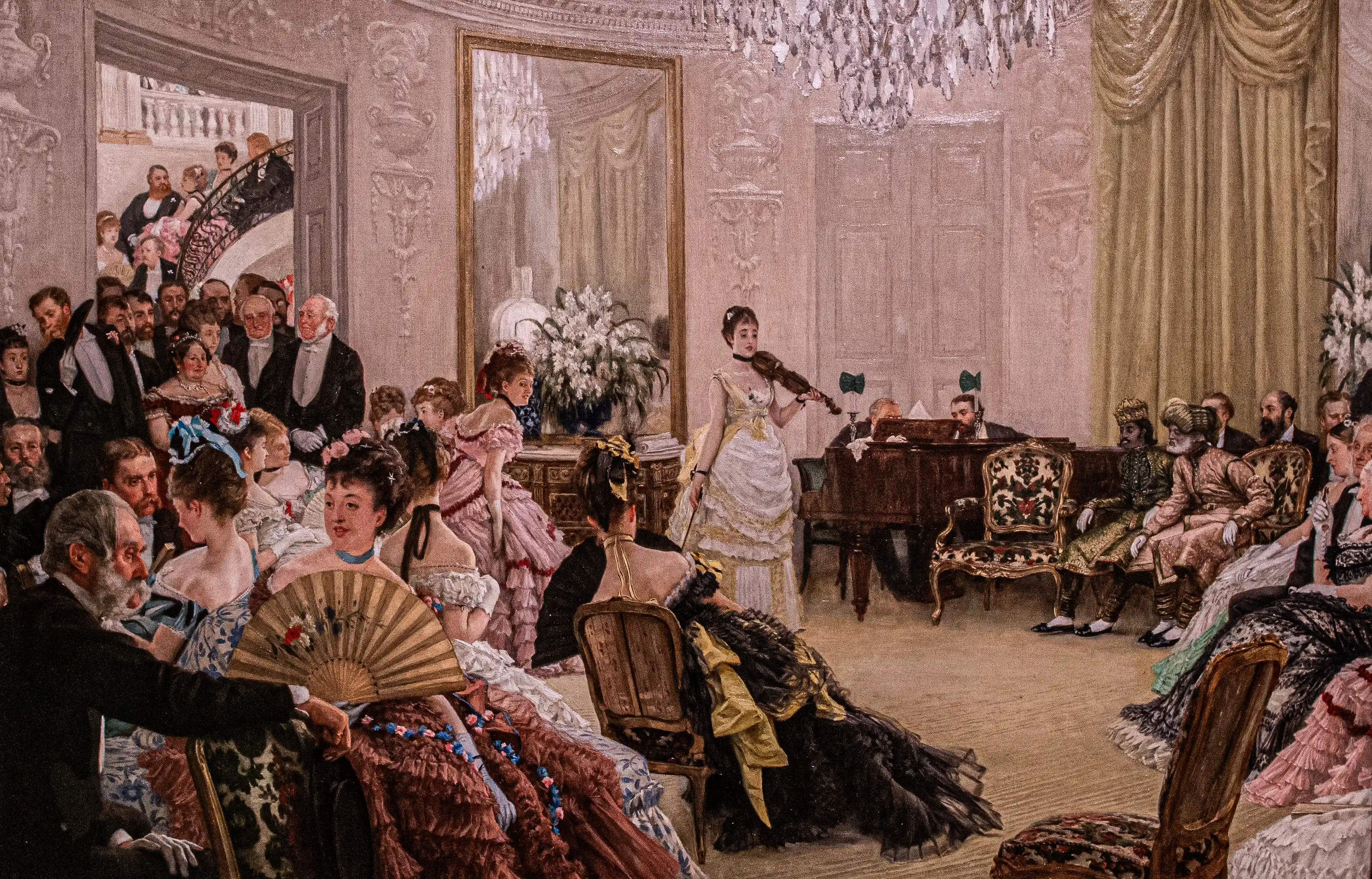 Guests in period clothing seated in a grand hall as a musician performs near a piano, with ornate walls and drapery in the background