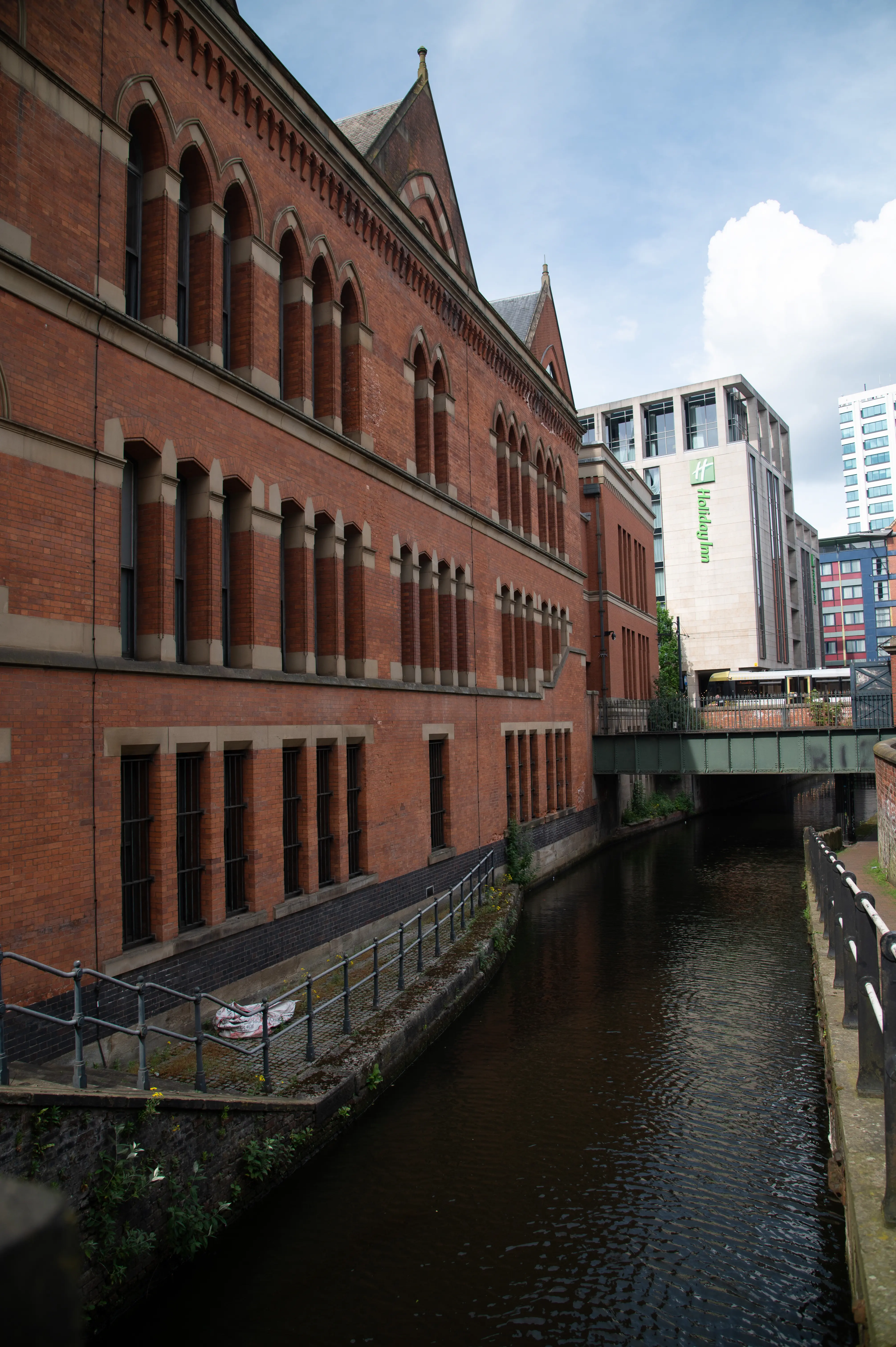 Red-brick buildings along a narrow canal with a modern hotel and green “Hilton” sign seen ahead.  