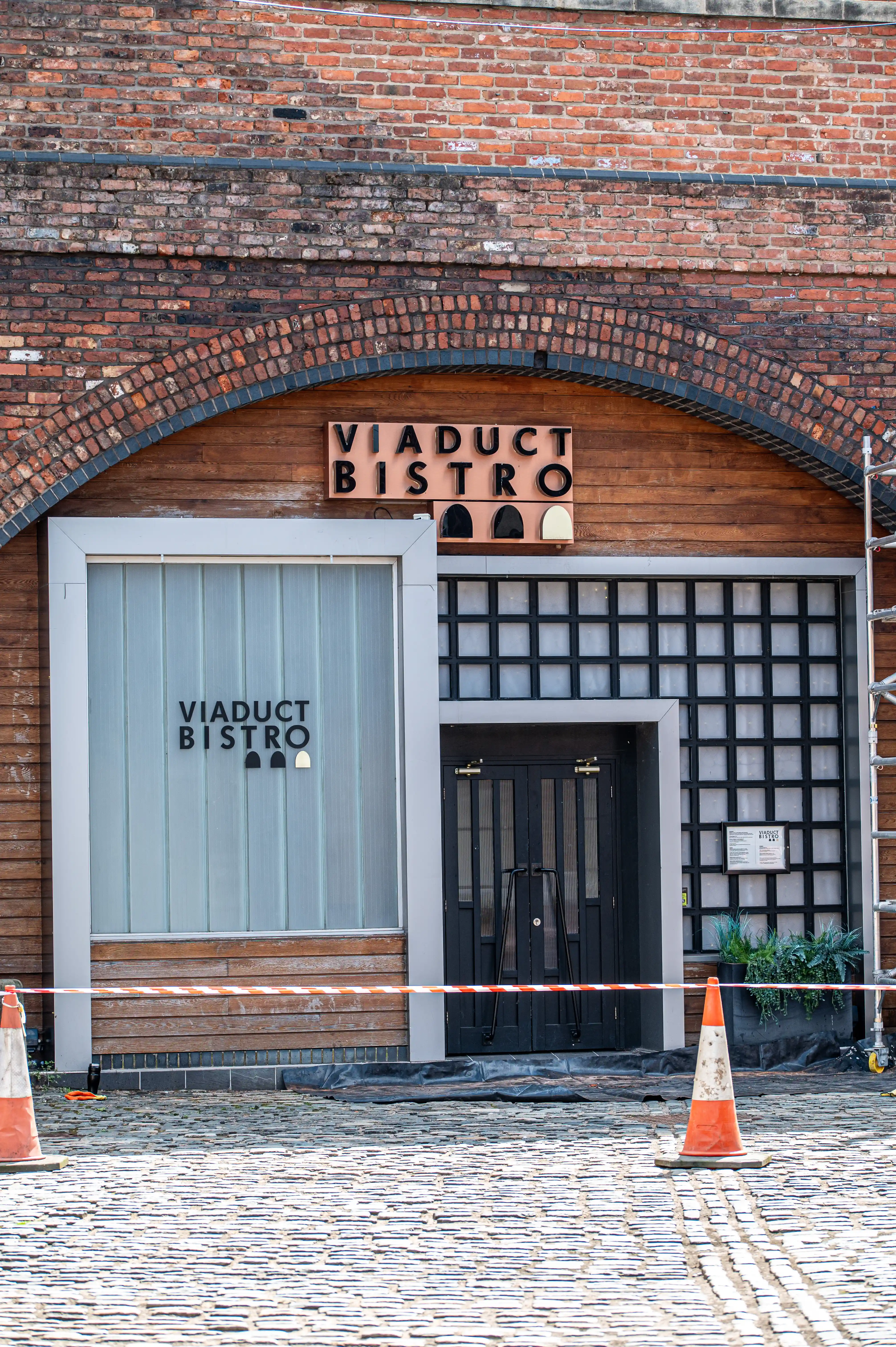 Entrance to Viaduct Bistro in a brick archway with a “VIADUCT BISTRO” sign above the door and orange safety cones in front.  