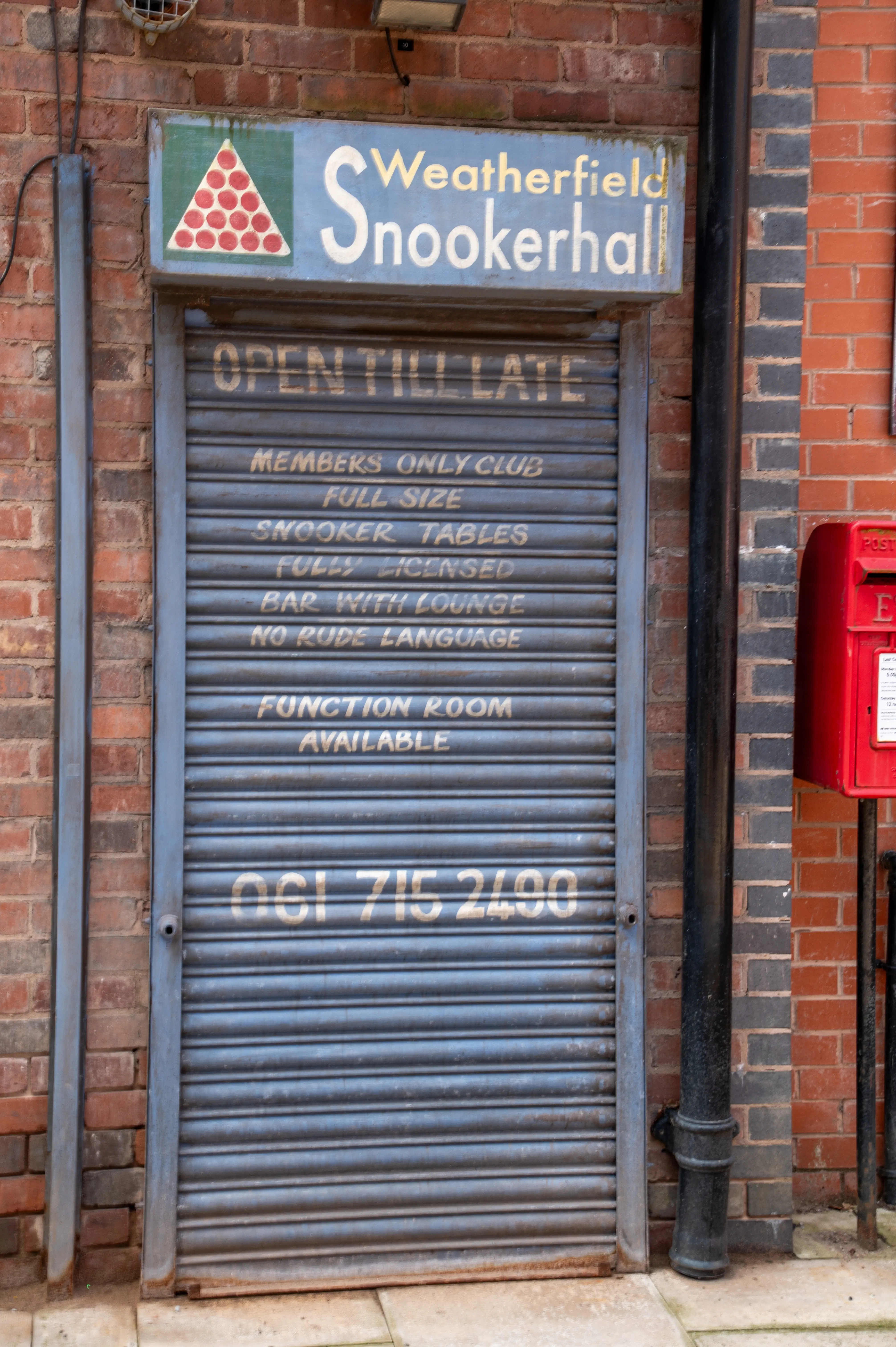 A closed metal roller shutter door for Weatherfield Snookerhall, with signs above and on the door listing club details and a phone number.