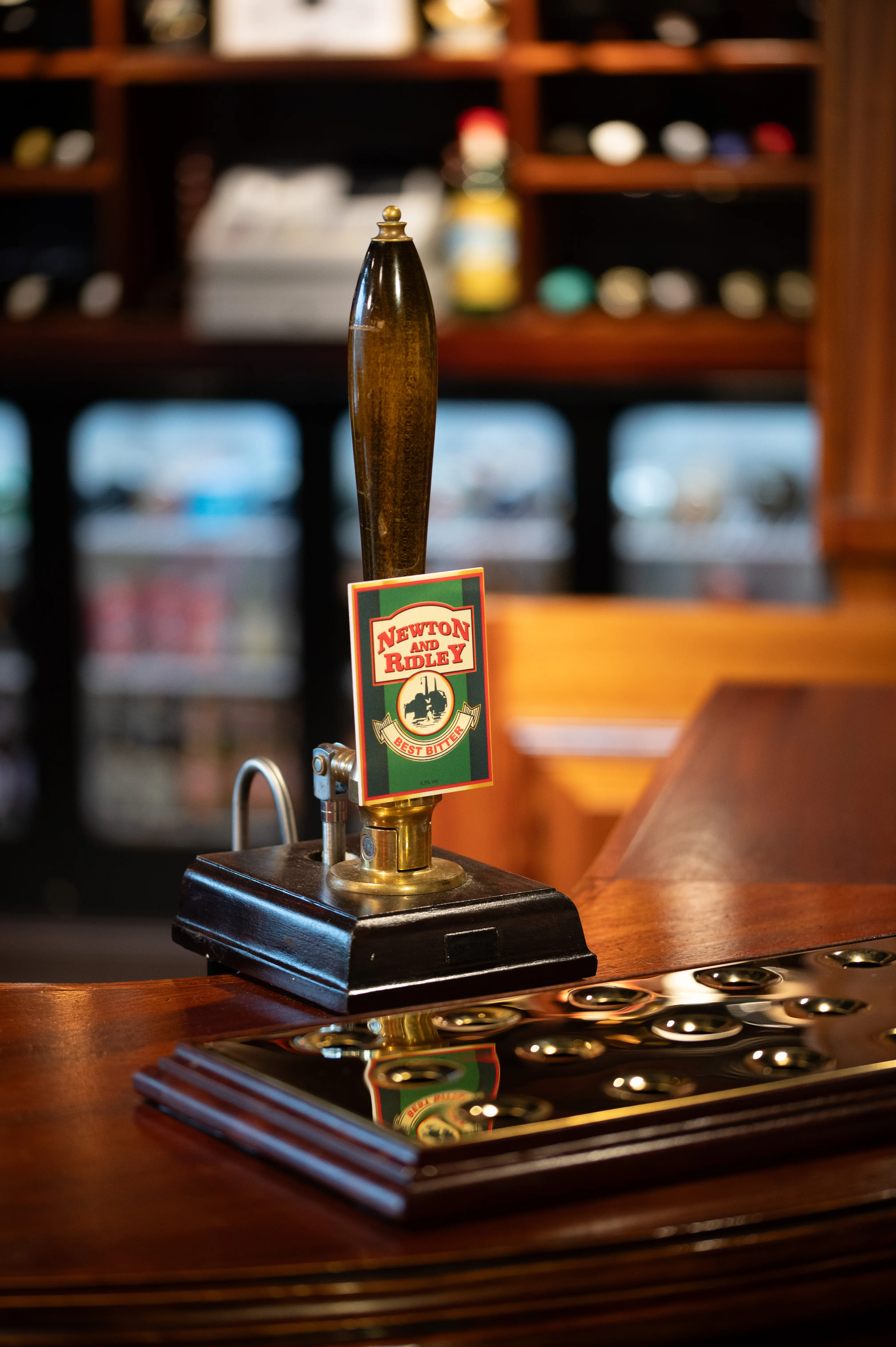A close-up shot of a dark wooden beer tap handle with a rectangular sign featuring the 