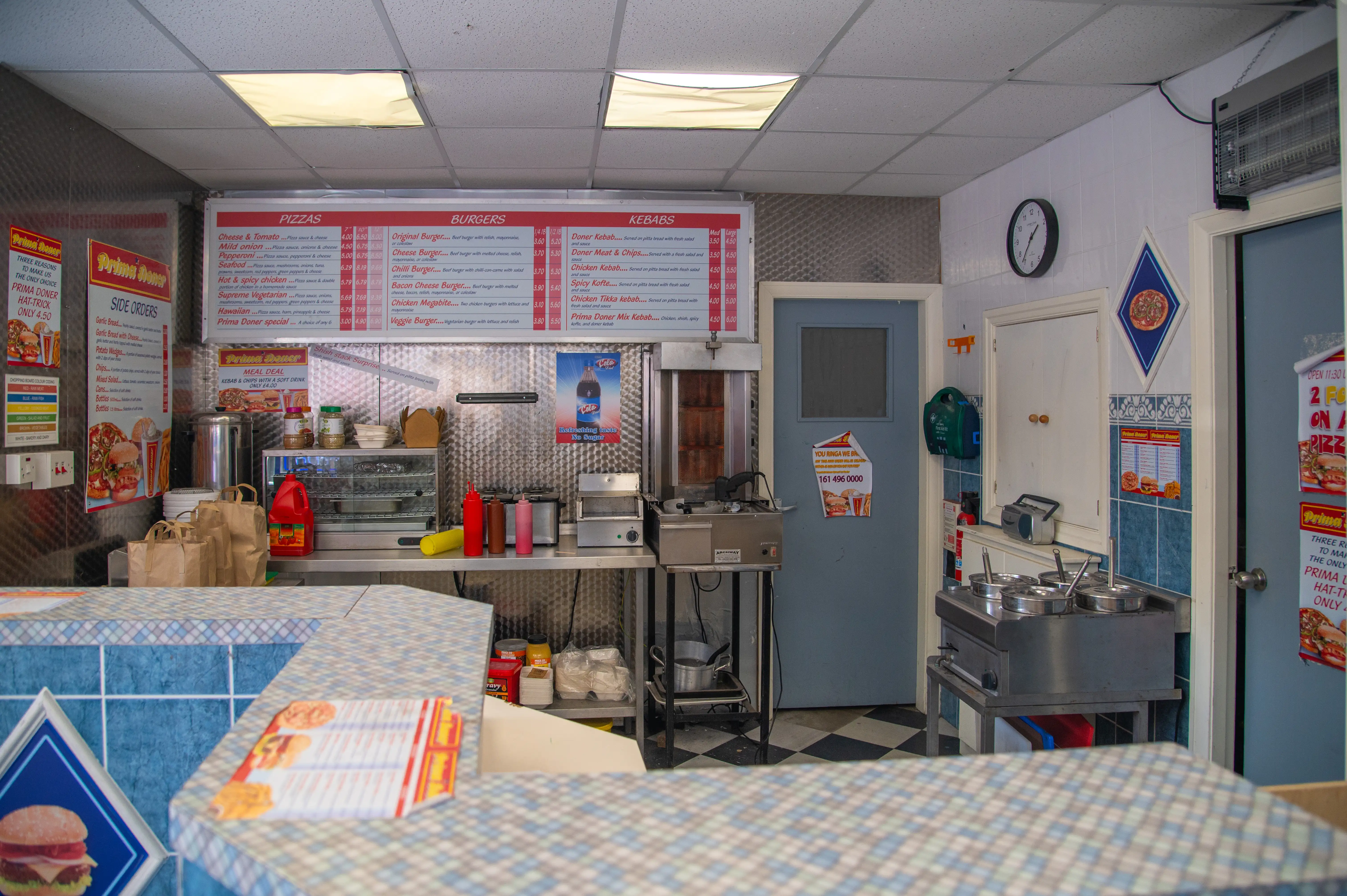 Interior view of a takeaway food shop with menus, counter, cooking equipment, and checkered floor.