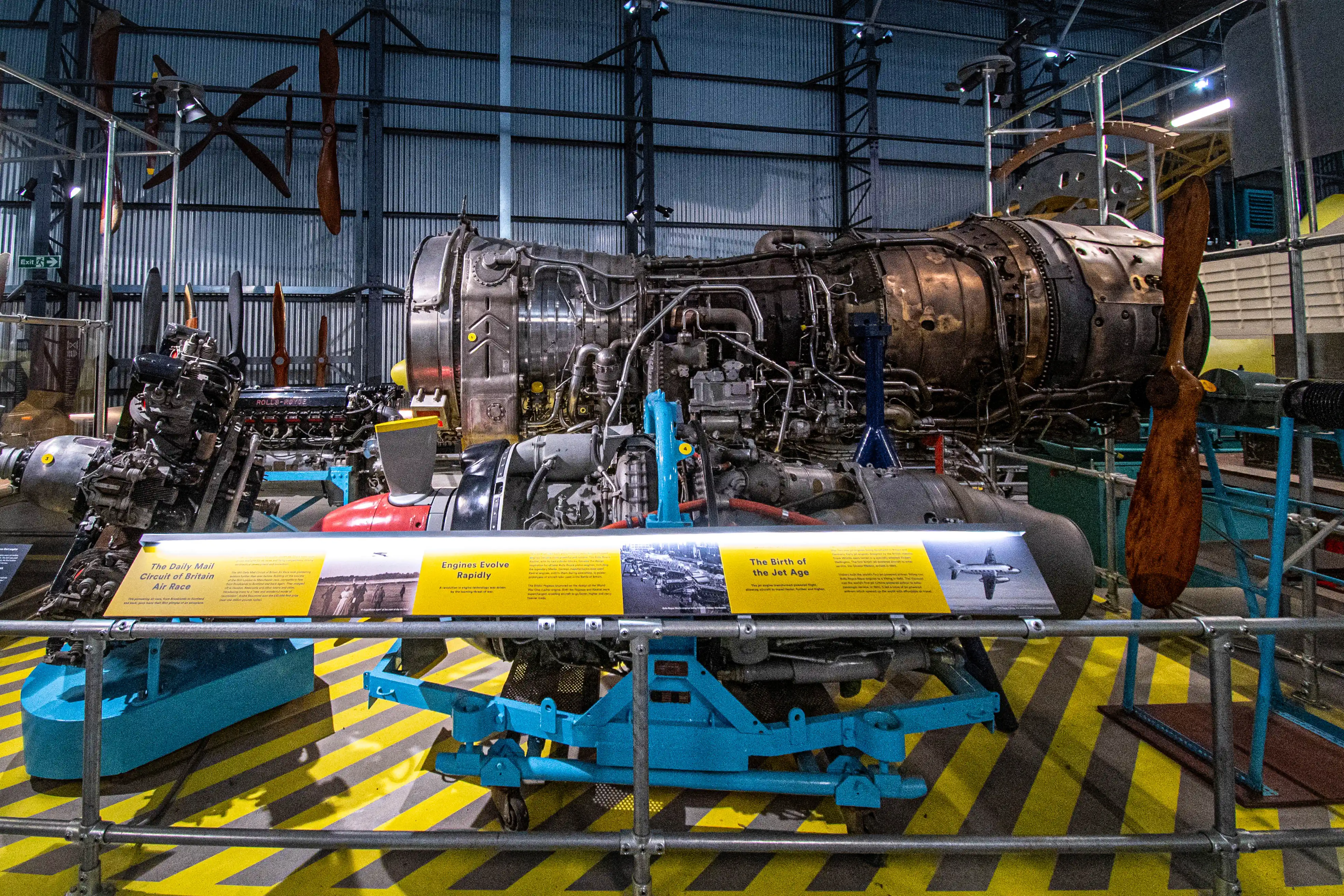 A detailed view of historical aircraft engines, including a large jet engine, displayed in a museum. Informational placards explain the evolution of engines and the beginnings of the Jet Age.