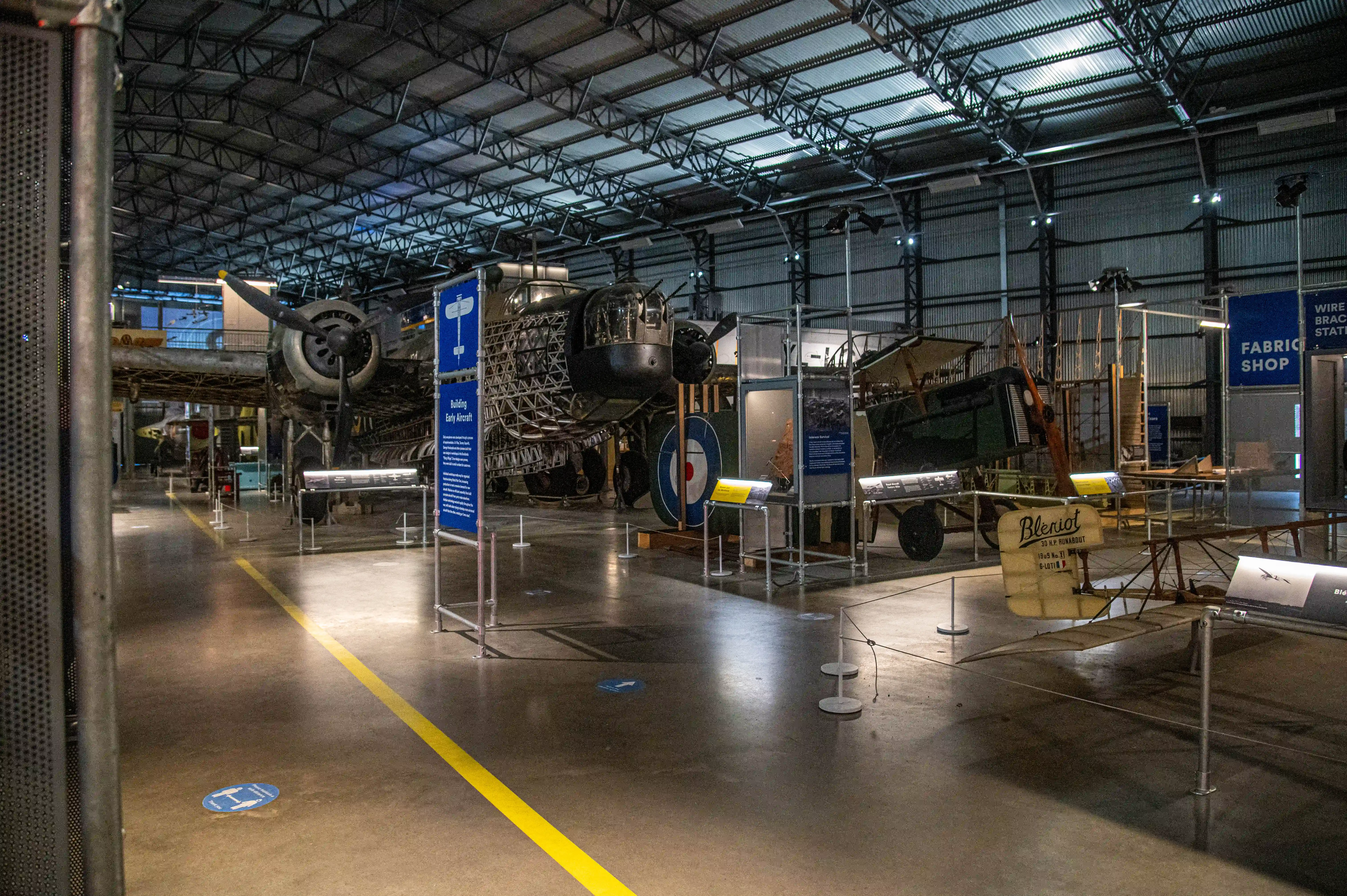 Interior view of an aviation museum with a large bomber aircraft and a Blériot biplane on display, with informational exhibits and industrial architecture.