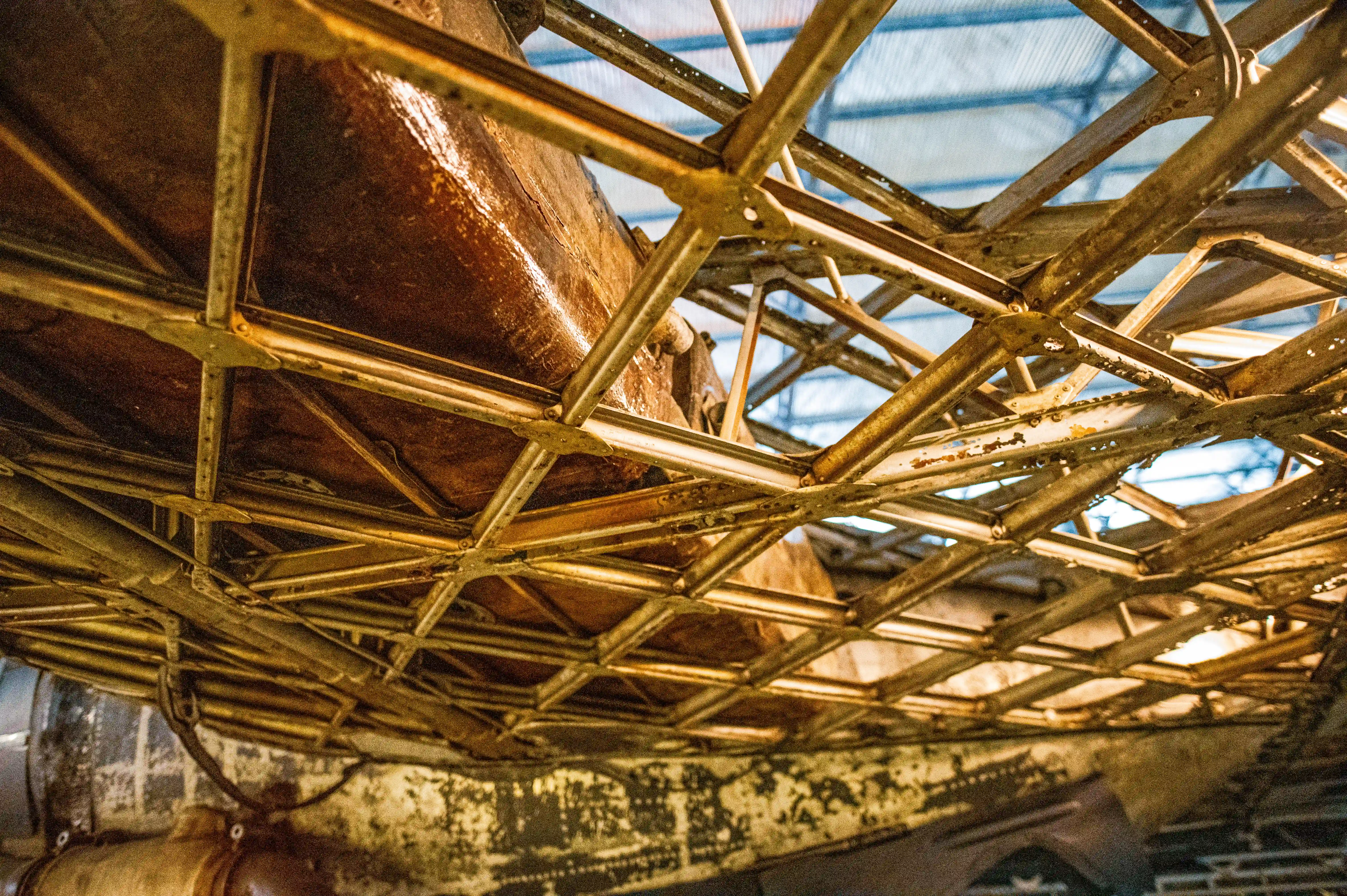 A detailed shot of the internal metallic structure of an aircraft, showing a grid of interconnected golden struts and beams, with brown material and signs of age visible underneath.