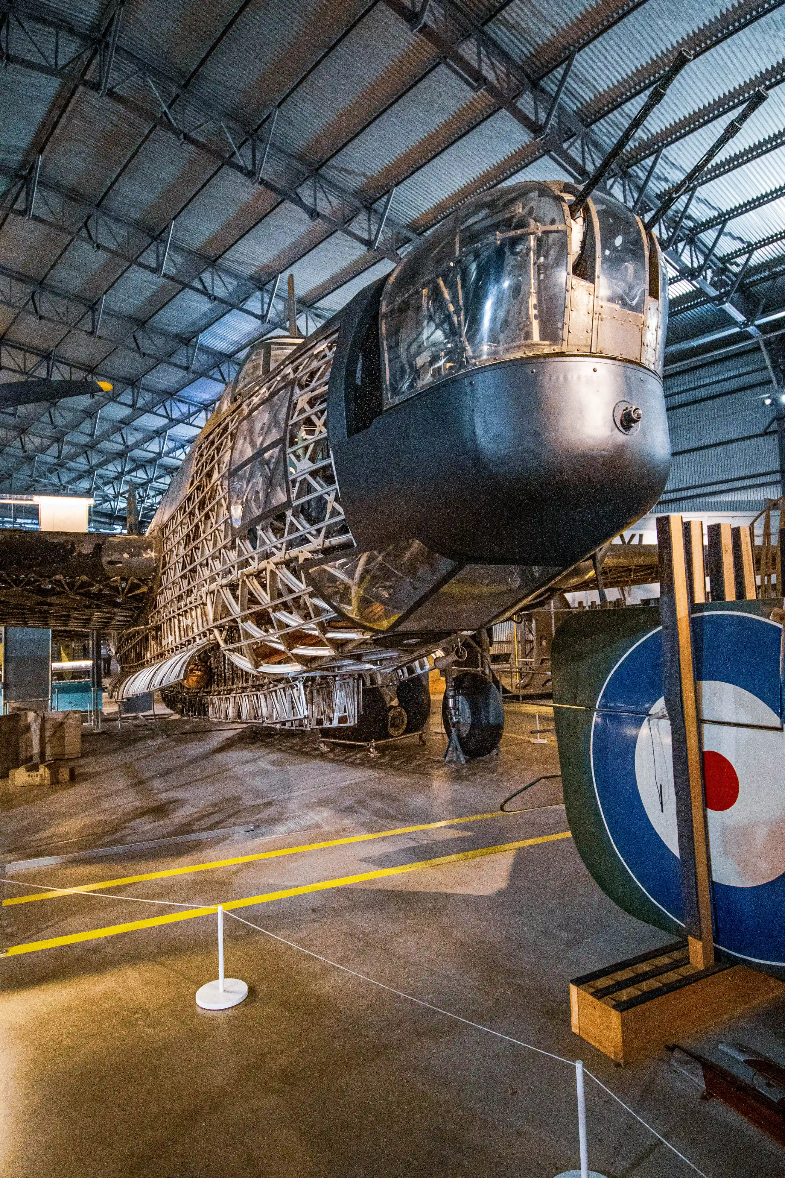 Partially restored Vickers Wellington bomber aircraft's interior structure, nose turret, and landing gear, with a Royal Air Force roundel display in the foreground, inside a museum hangar.