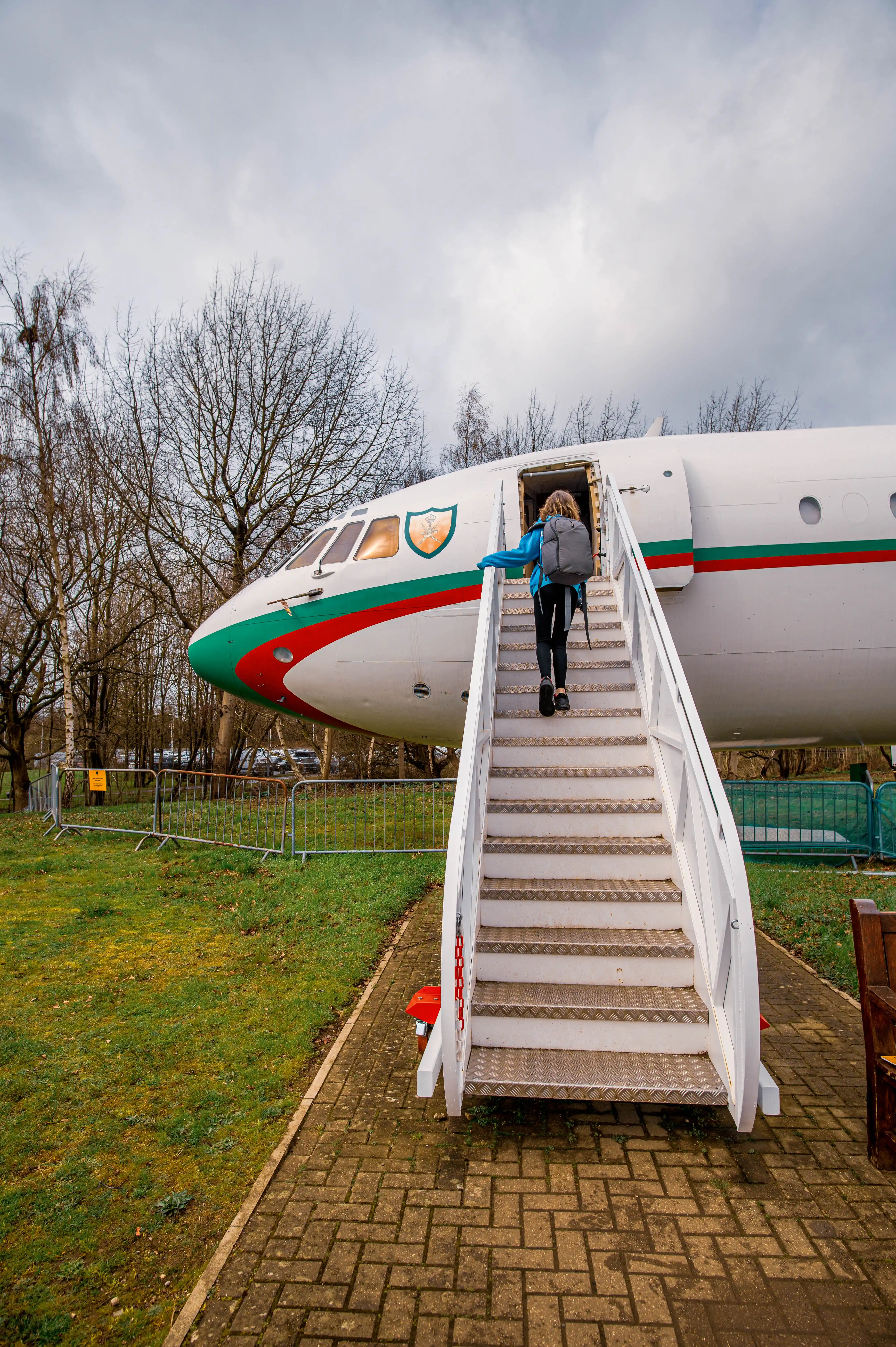 A vintage airplane with a set of stairs leading up to its open door, set against a backdrop of trees and a cloudy sky.