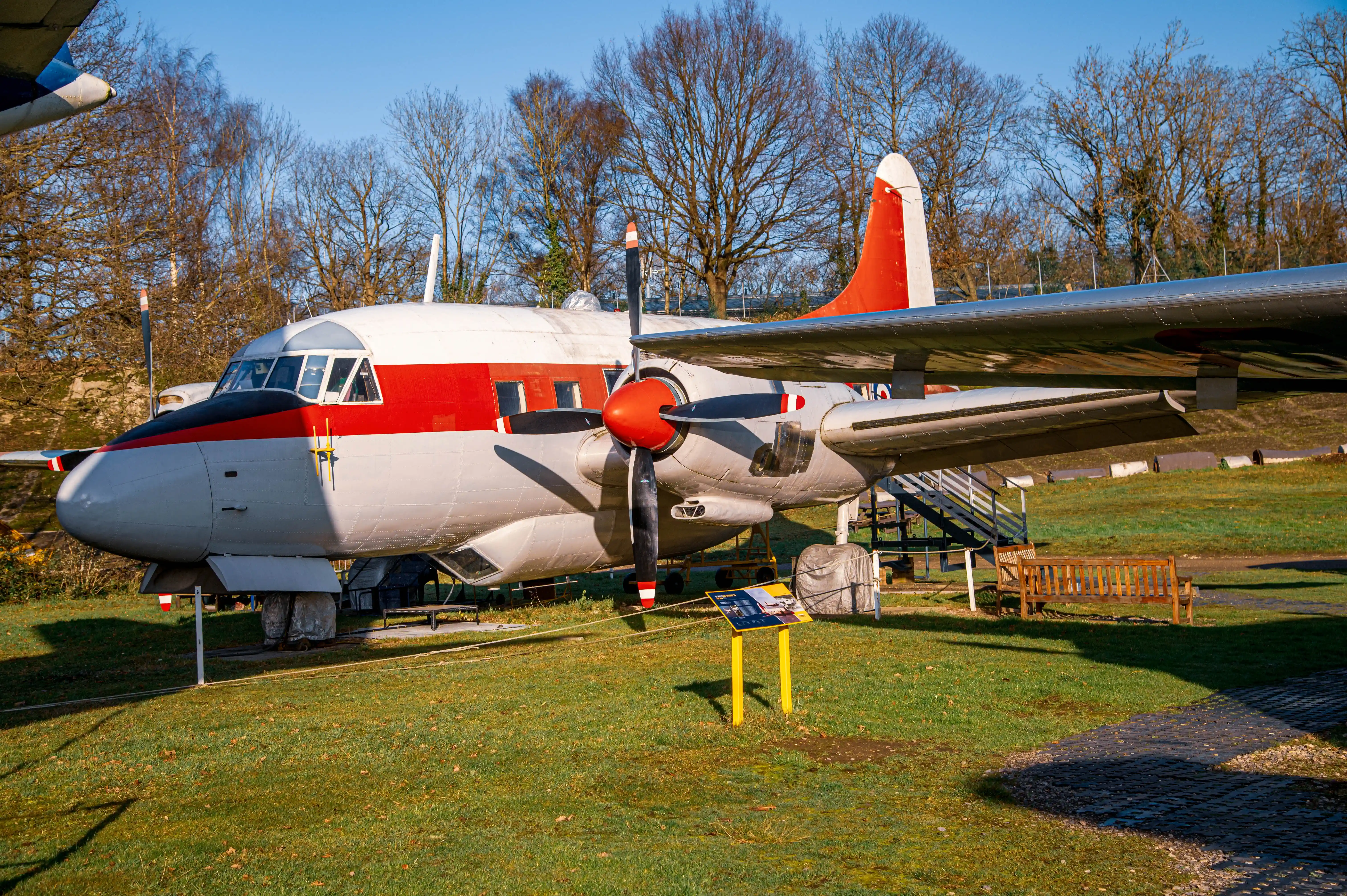 Side view of a vintage turboprop airplane with red and white markings parked on a lawn with trees in the background.