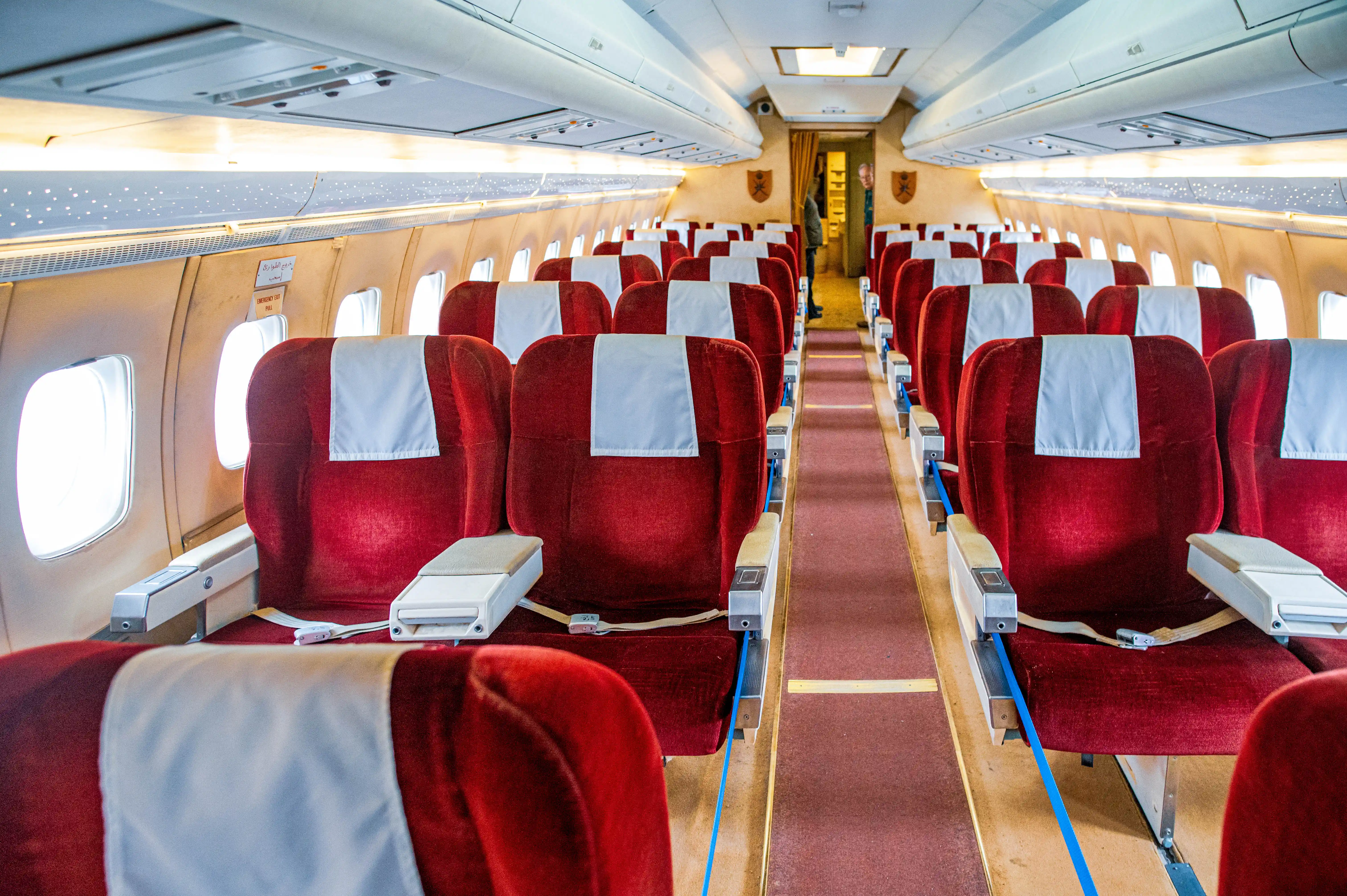  Interior view of an empty airplane cabin with rows of red velvet passenger seats and white headrests, looking down the aisle.