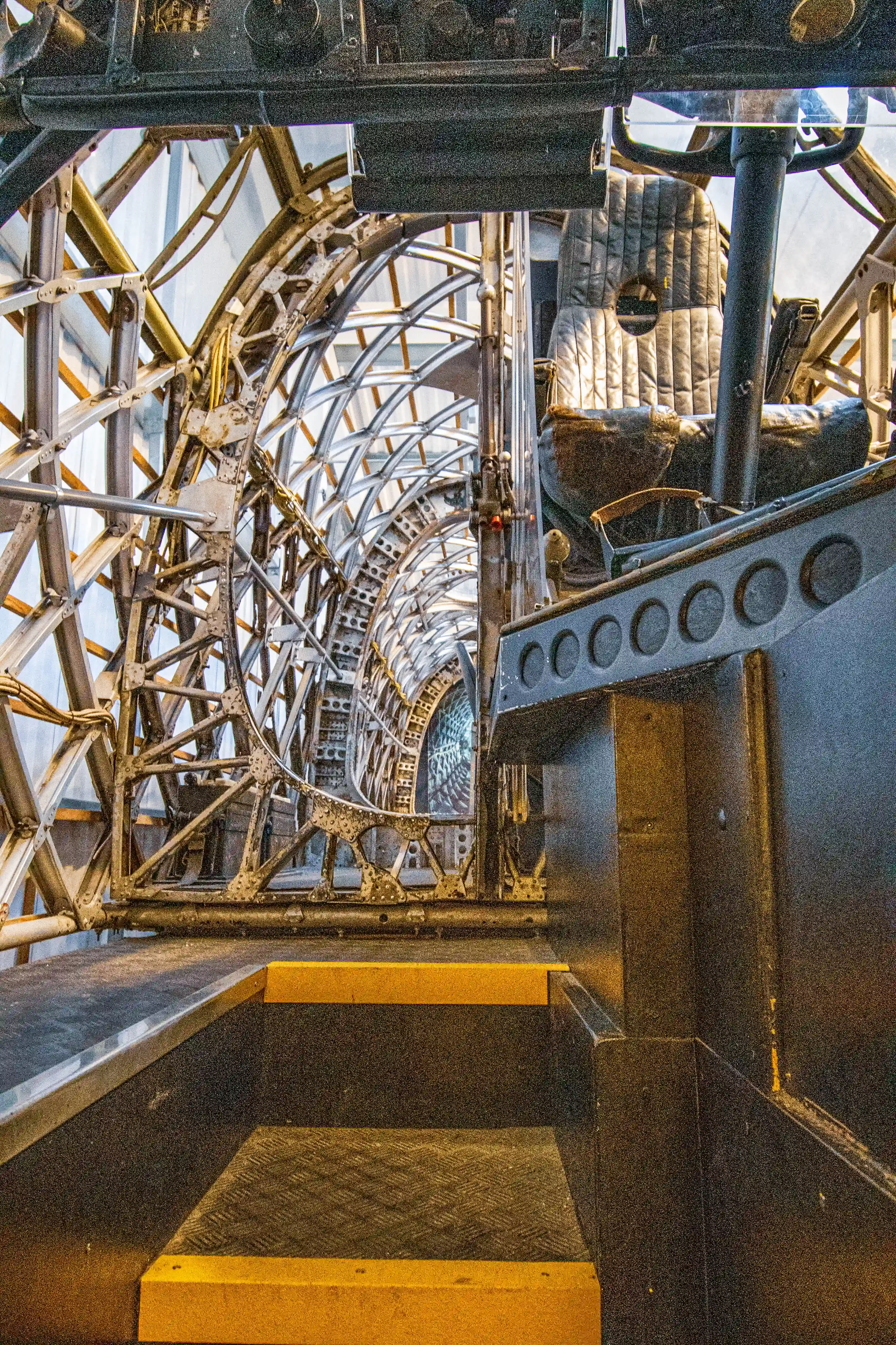 A detailed view of the undercarriage and internal mechanics of an aircraft, showcasing a complex framework of metal beams, pipes, and structural supports. The image highlights the engineering precision and industrial design of the aircraft's underbelly, with visible hydraulic systems, wiring, and landing gear components. The scene is captured from below