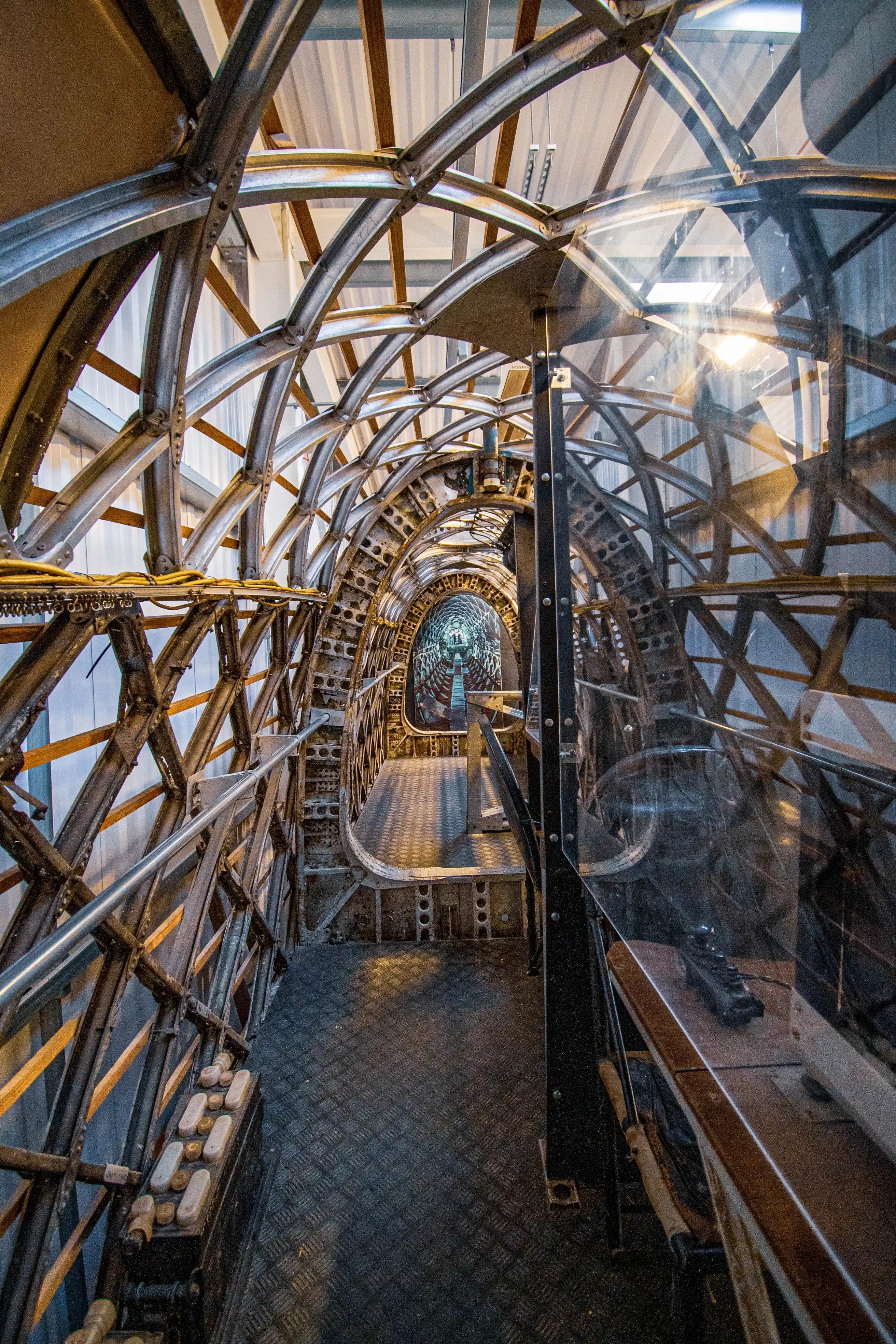Interior of an aircraft showing the detailed metal framework, ribbed ceiling, and diamond-plate flooring, with a perspective looking down a corridor-like section.
