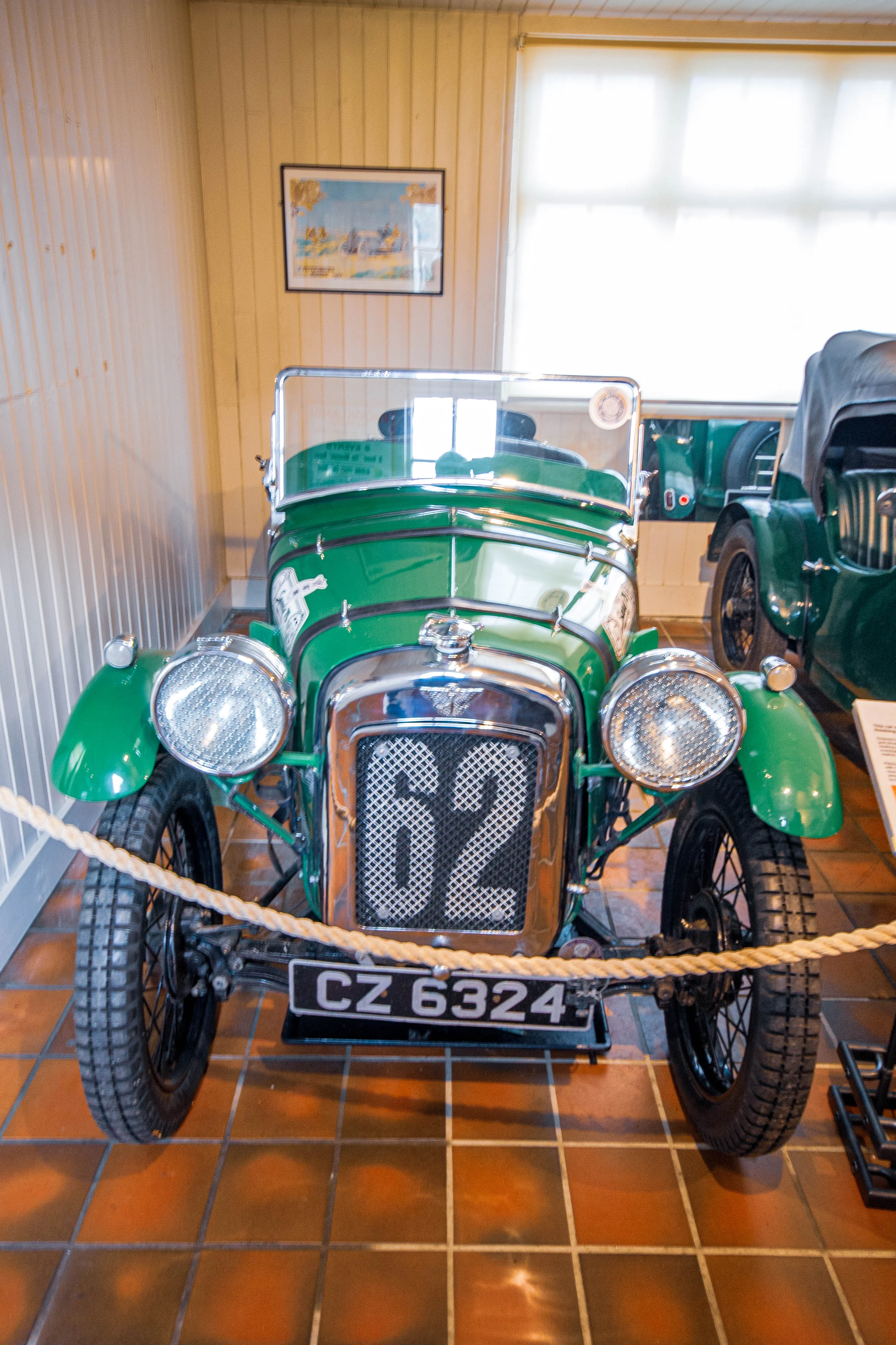 A front view of a classic green car with large round headlights, a chrome grille displaying the number 62, and a UK license plate reading CZ 6324.