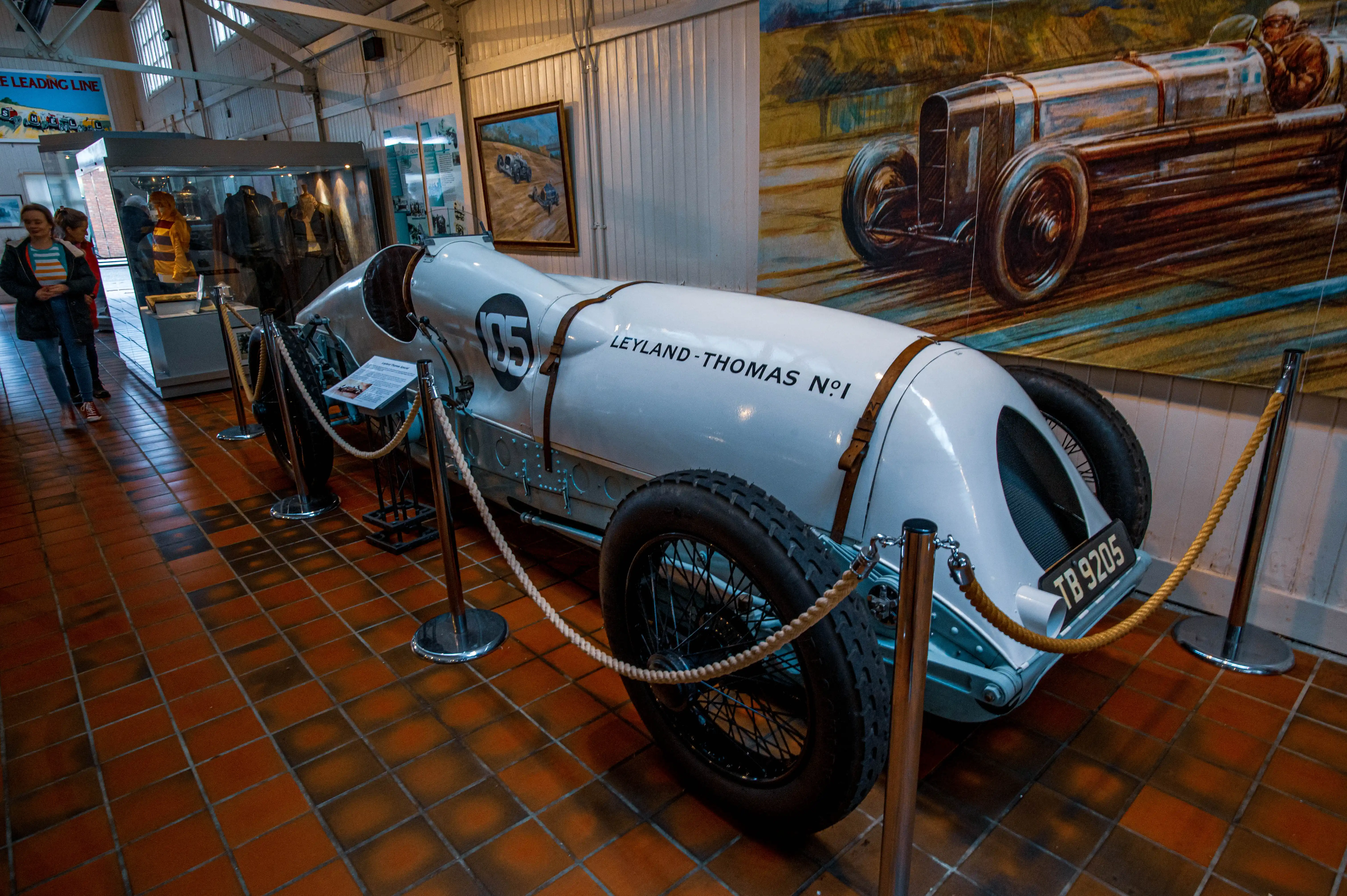  A white vintage racing car named Leyland-Thomas No. 1 with the number 05 on its side, displayed on a tiled floor in a museum.