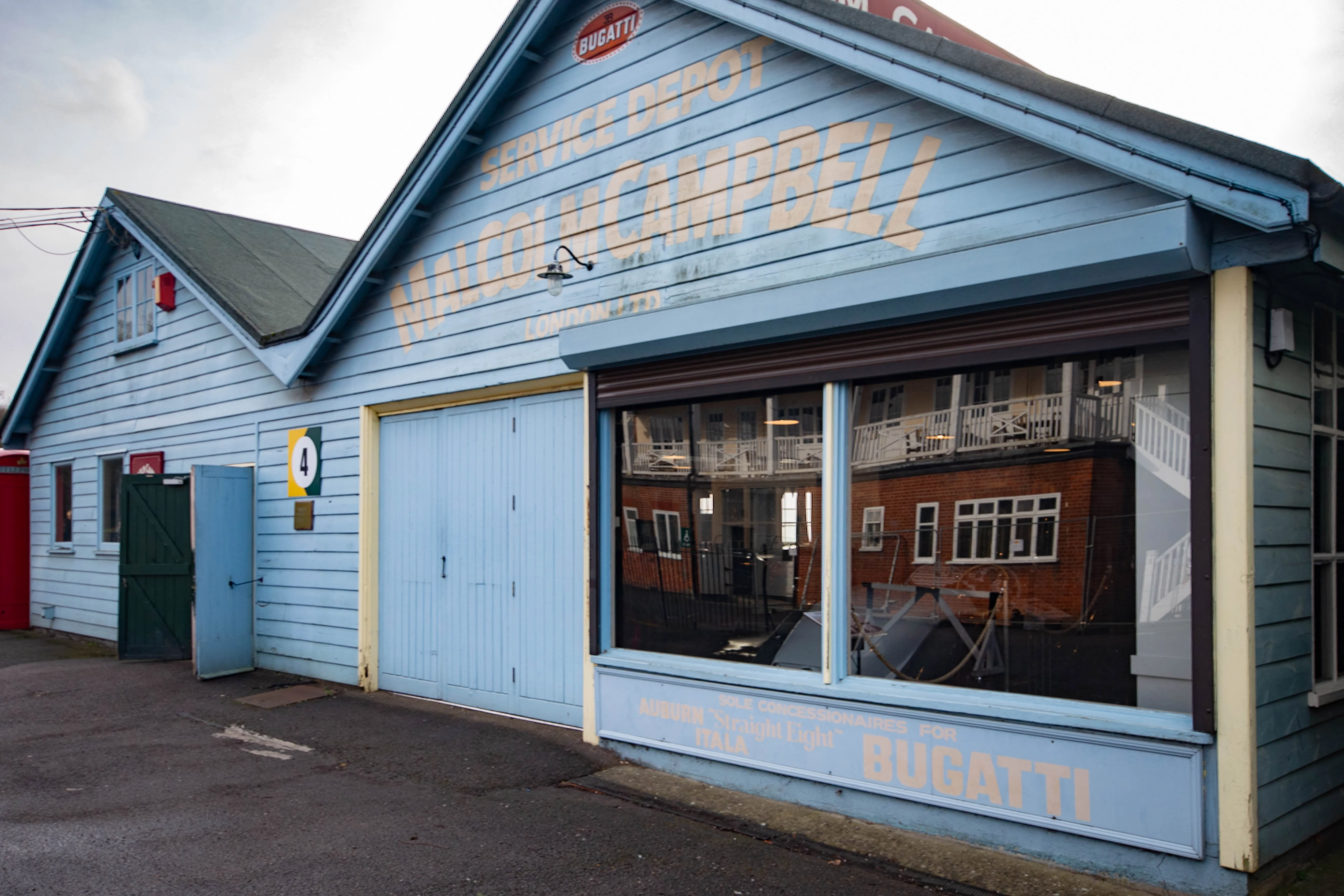 Exterior view of a light blue wooden building, likely a former car service depot, with faded painted signage including &laquo;Bugatti&raquo