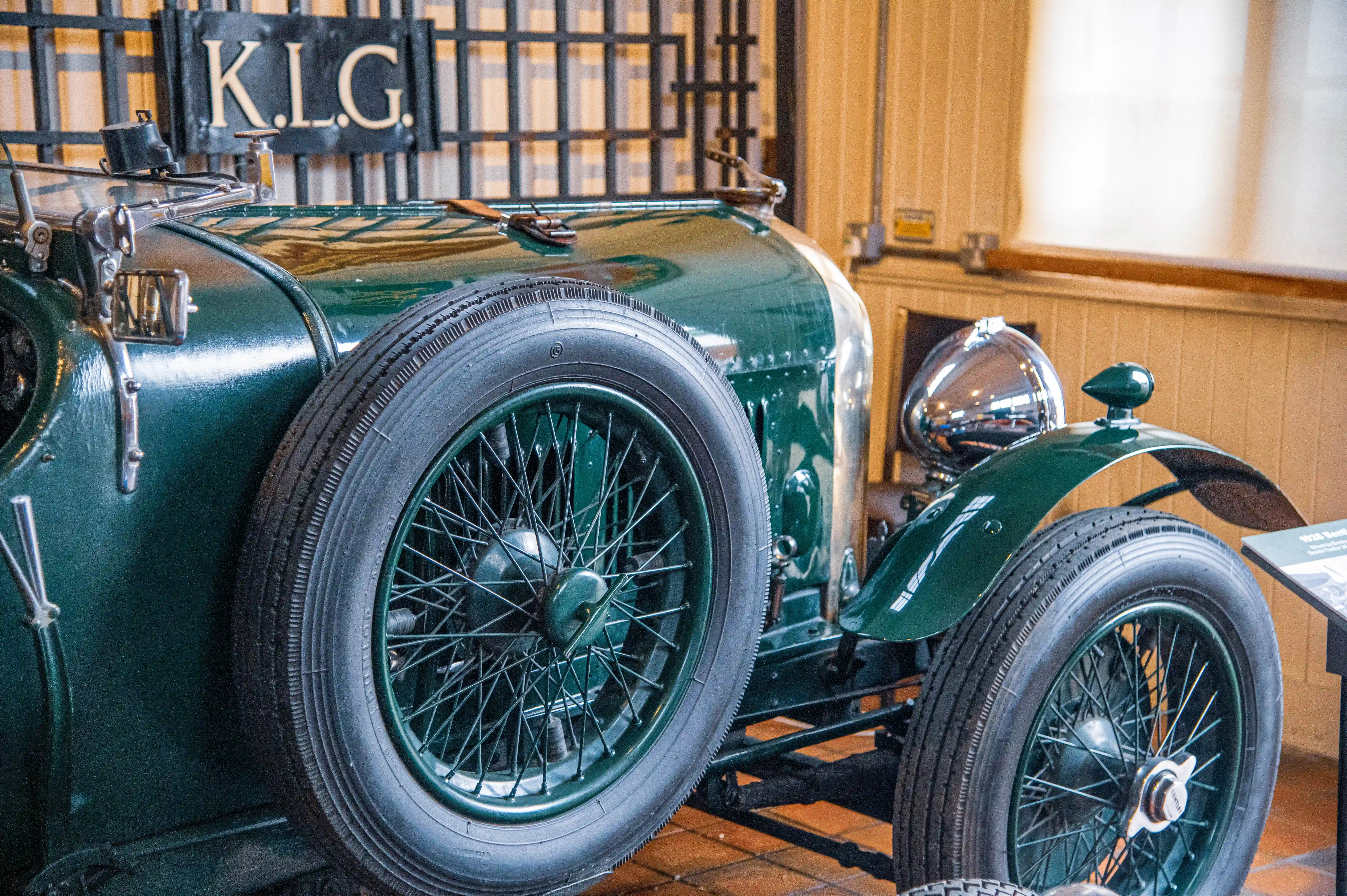 A detailed view of the front wheel and part of the bonnet of a vintage green Bentley car, with a wire-spoke wheel prominent