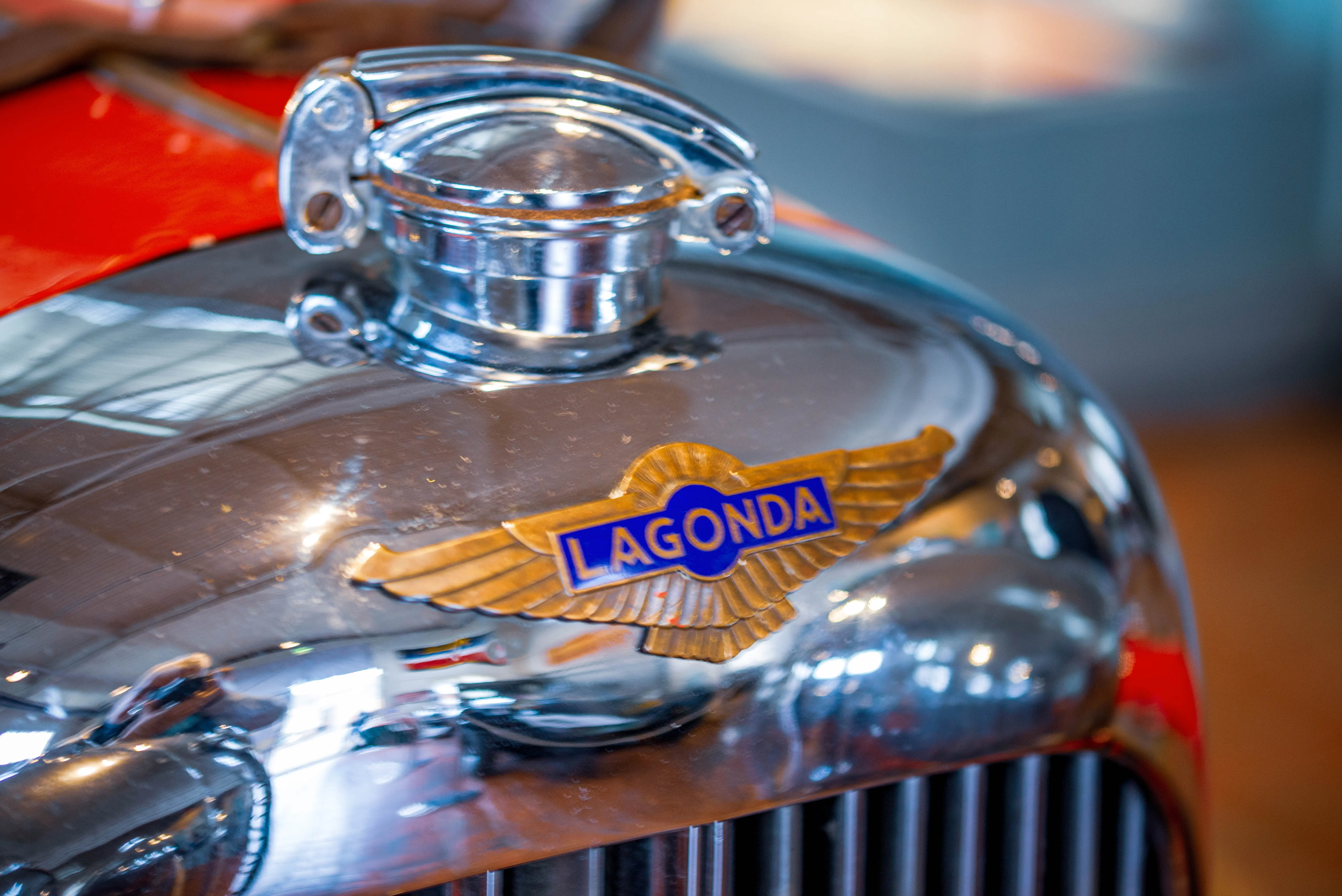 Close-up of a polished chrome car bonnet with a golden winged Lagonda badge.