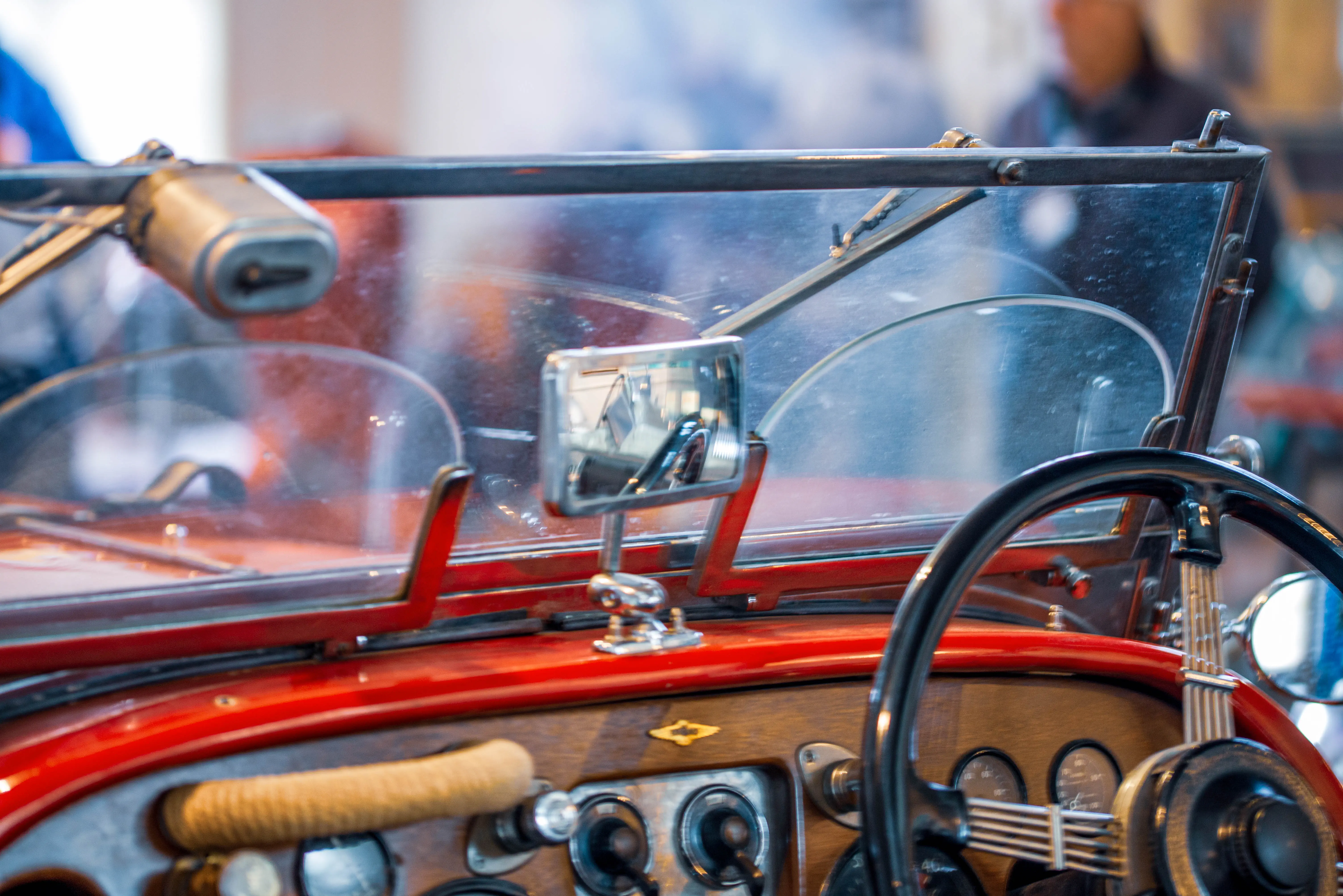 Close-up view of the interior of a vintage red convertible car, showing the dashboard with gauges, a steering wheel, and a rearview mirror.