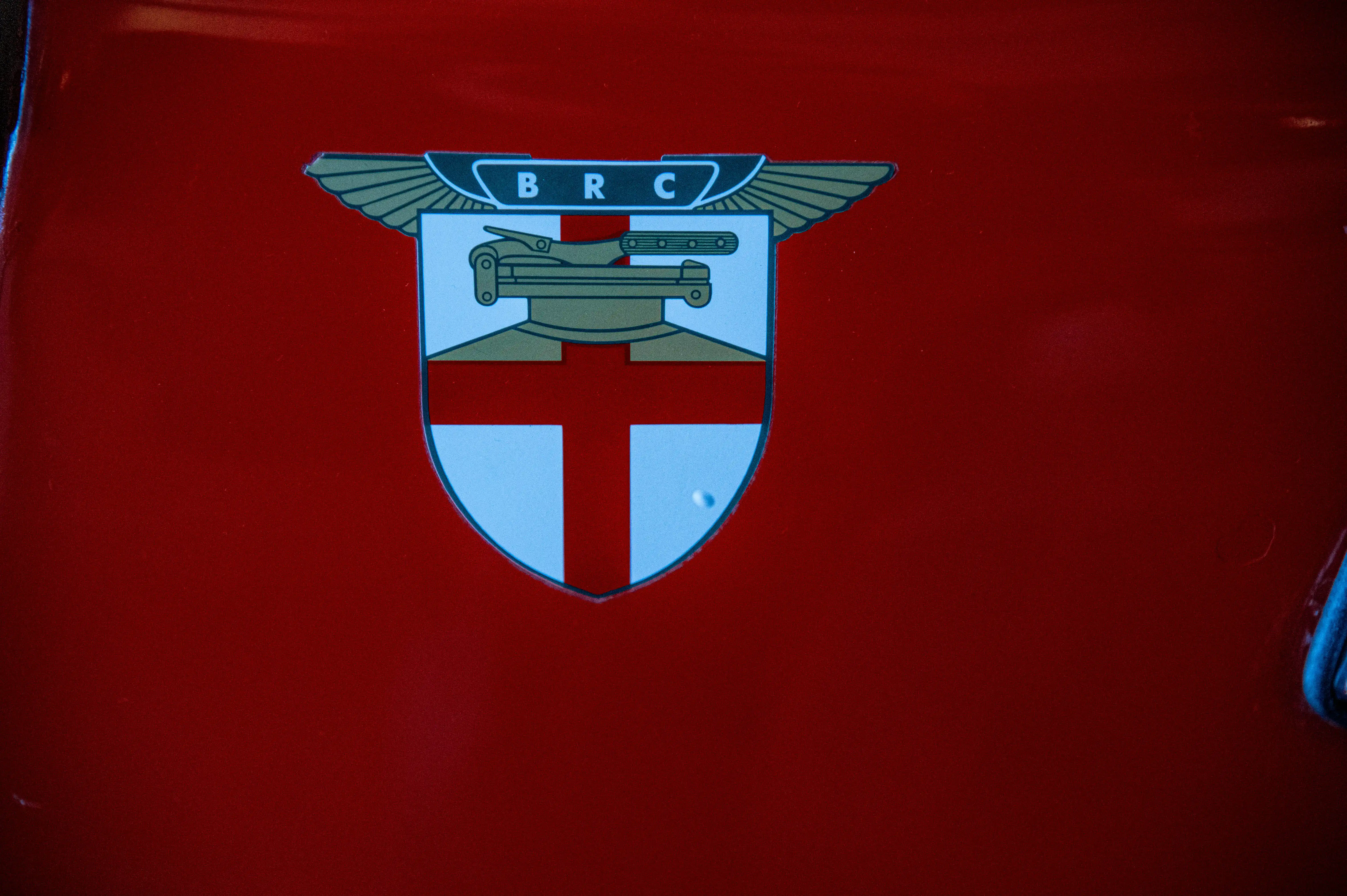 A detailed image of the BRC emblem, a crest with winged elements, a tank, and a cross, set against a glossy red surface.