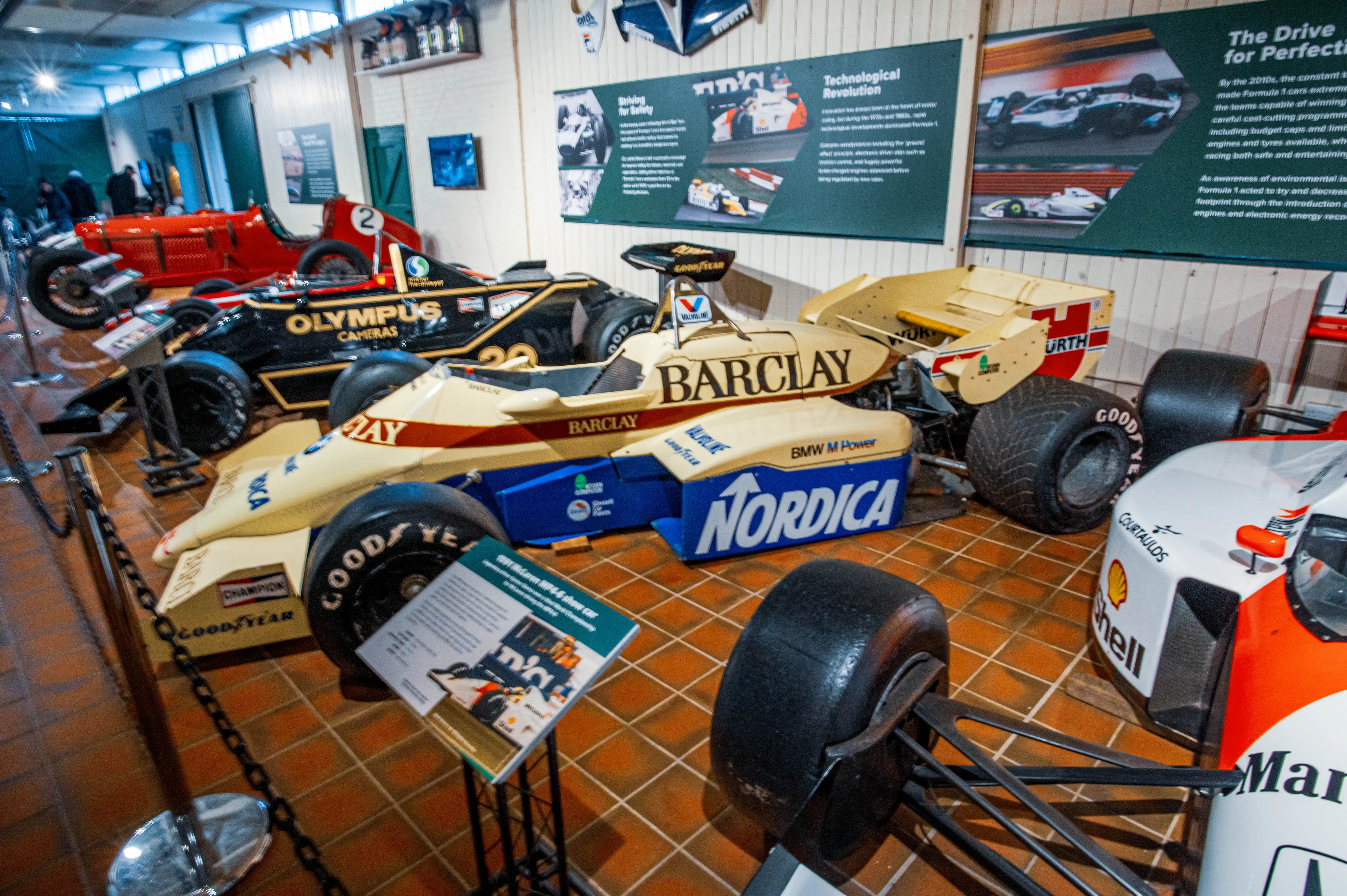 A museum display of several vintage Formula 1 racing cars, with a focus on the front section of a yellow and blue car with 