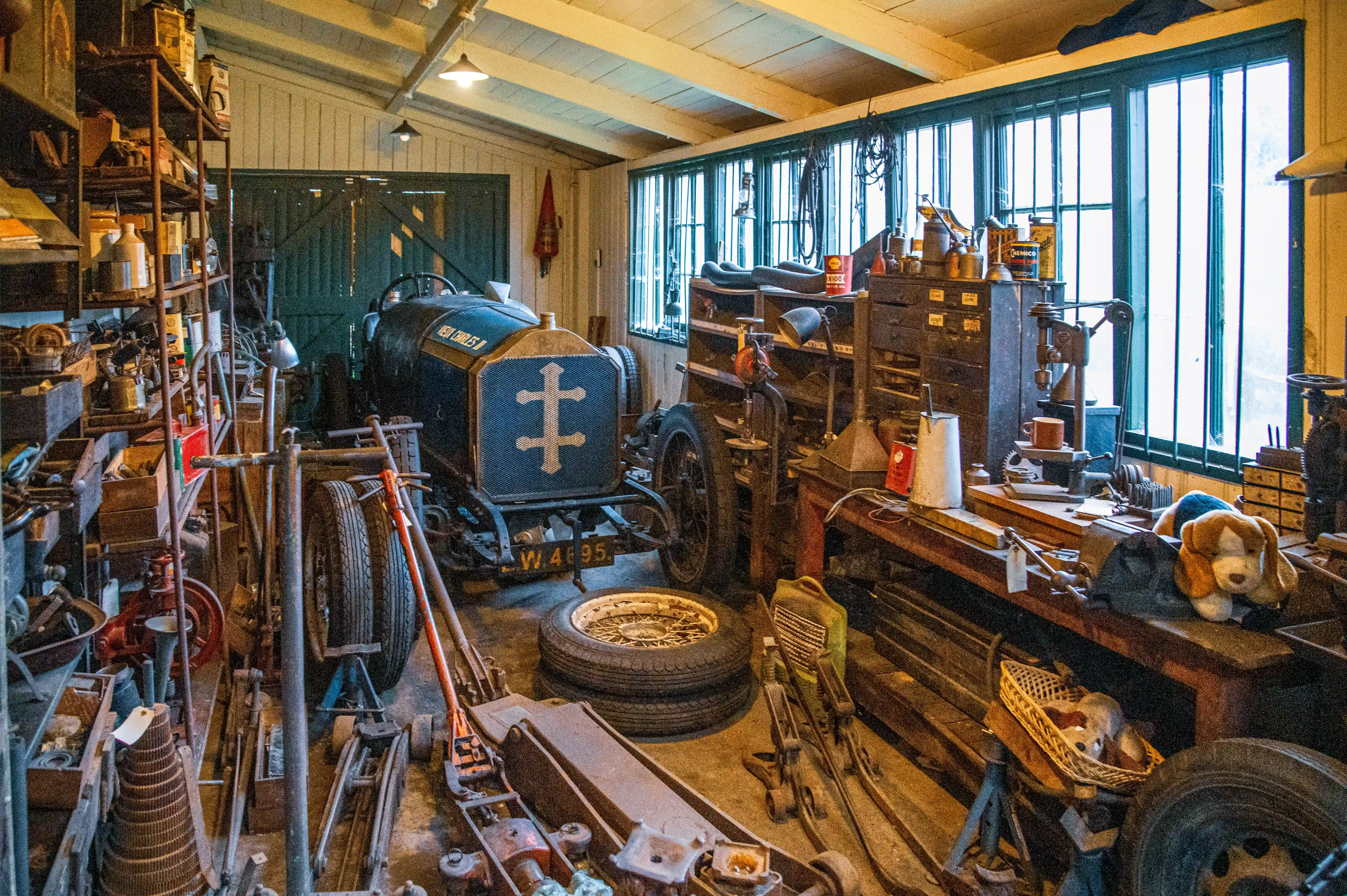 A vintage garage workshop filled with tools and spare parts, with a classic racing car in the centre.