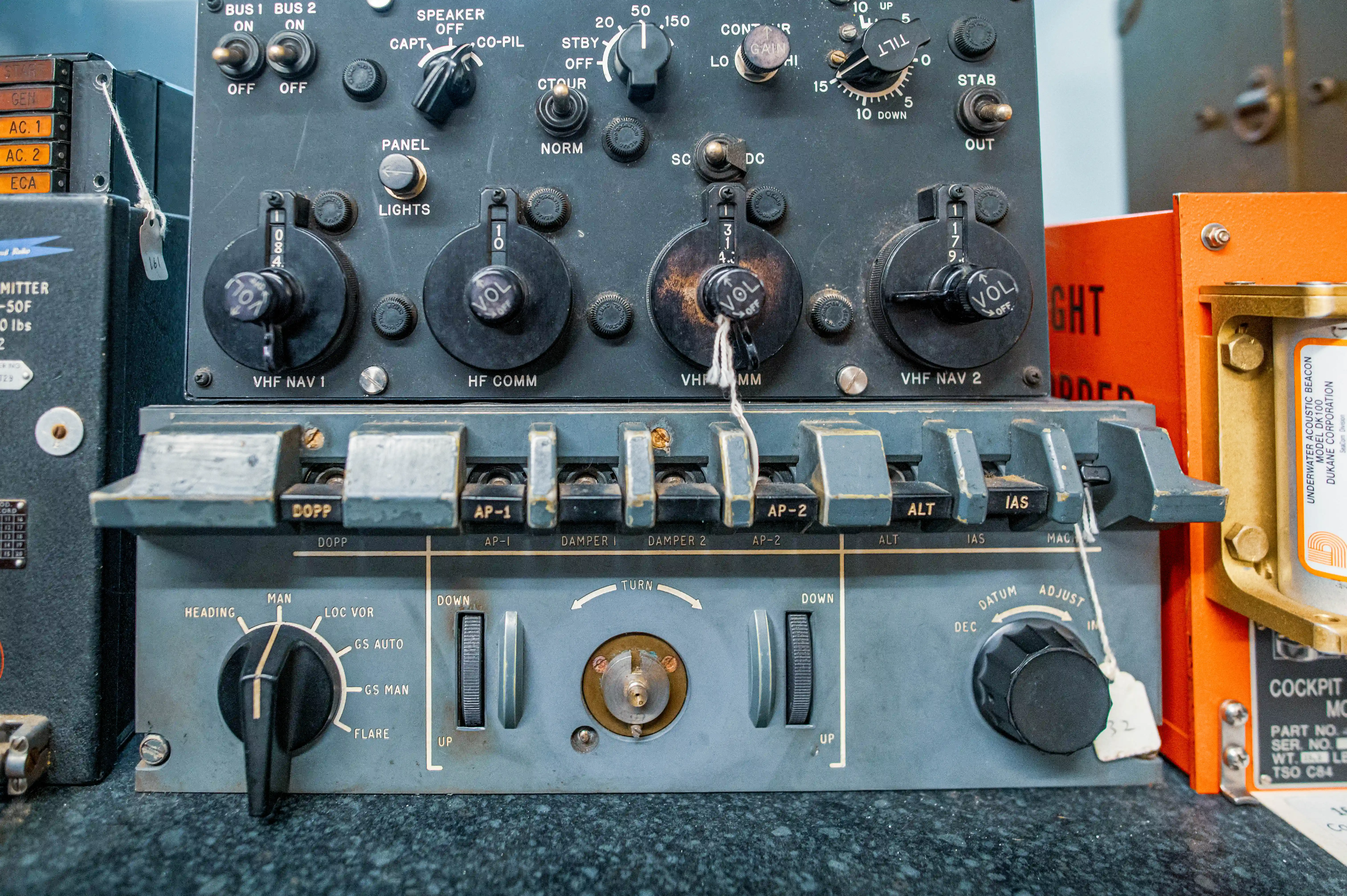 Two vintage radio receiver units are displayed side-by-side. The top unit has a large tuning dial and numerous smaller control knobs. The bottom unit features a large VU meter and a fused power switch. Both units appear to be constructed of metal with a grey finish and show signs of age.