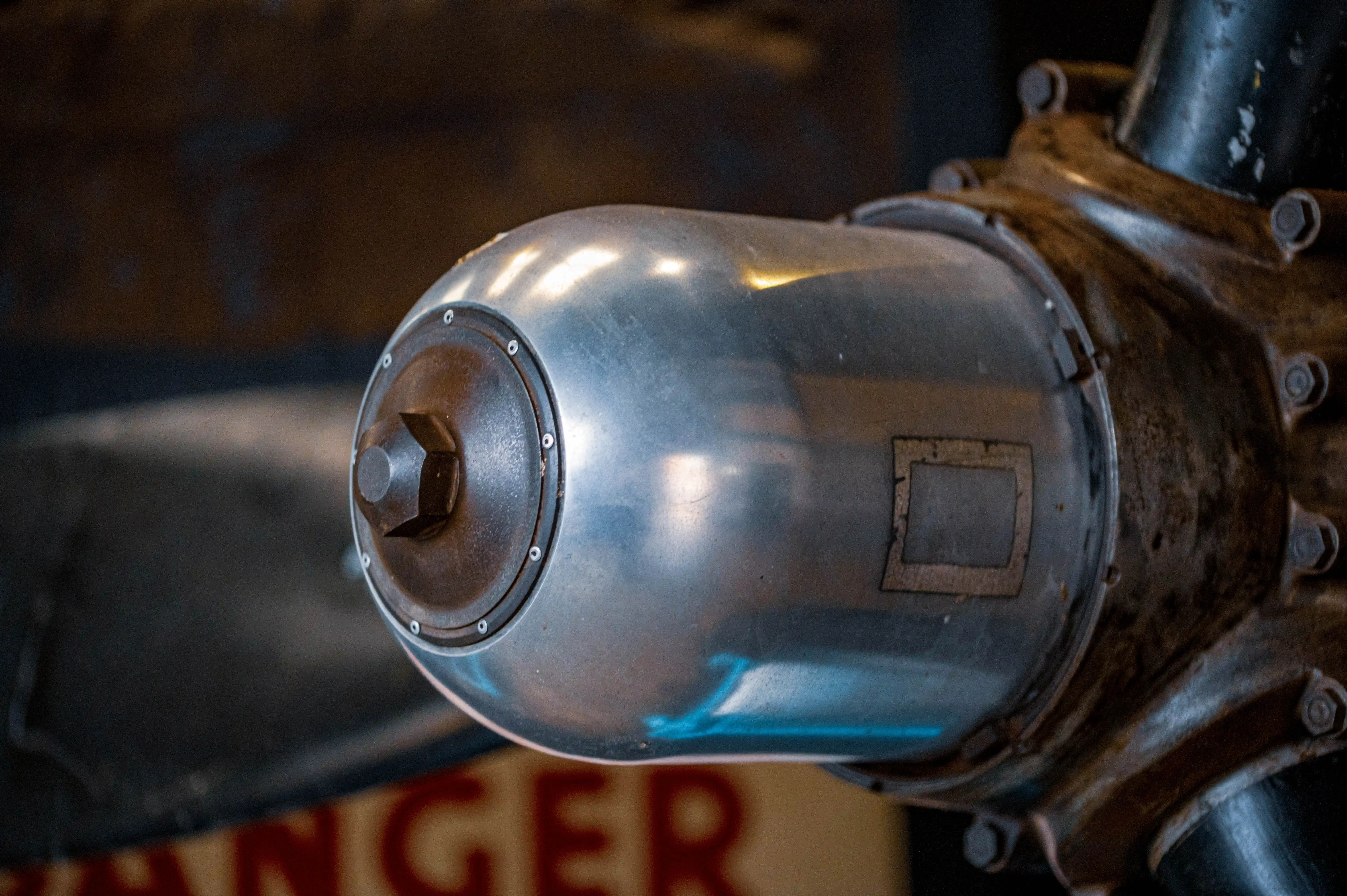 Close-up of the metallic hub of an aircraft propeller, showing the rounded silver dome and the bolted, rusty metal mounting.