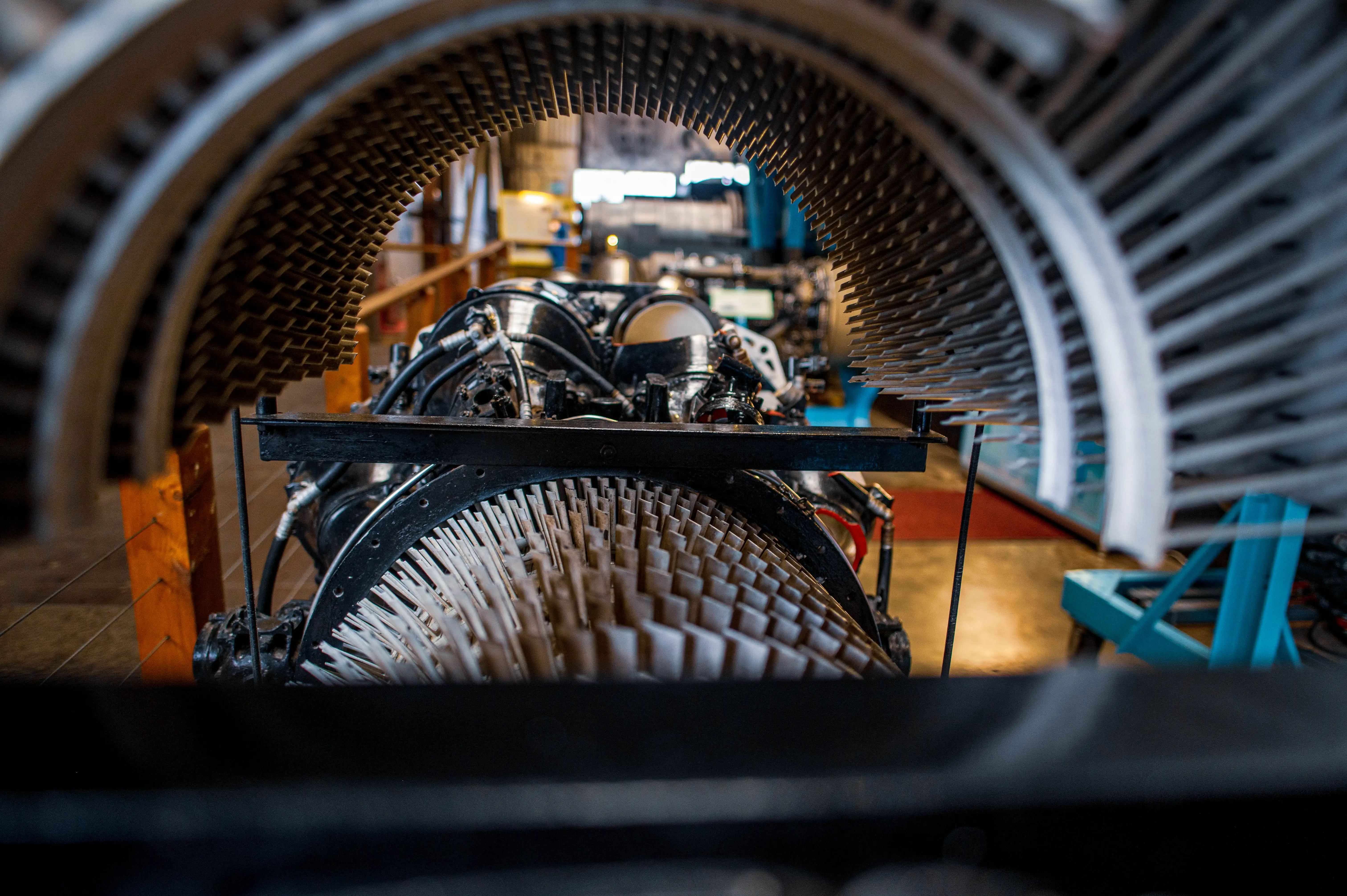 Close-up view of a jet engine's compressor blades, seen through the fan casing. Some visitors are visible in the blurred background.
