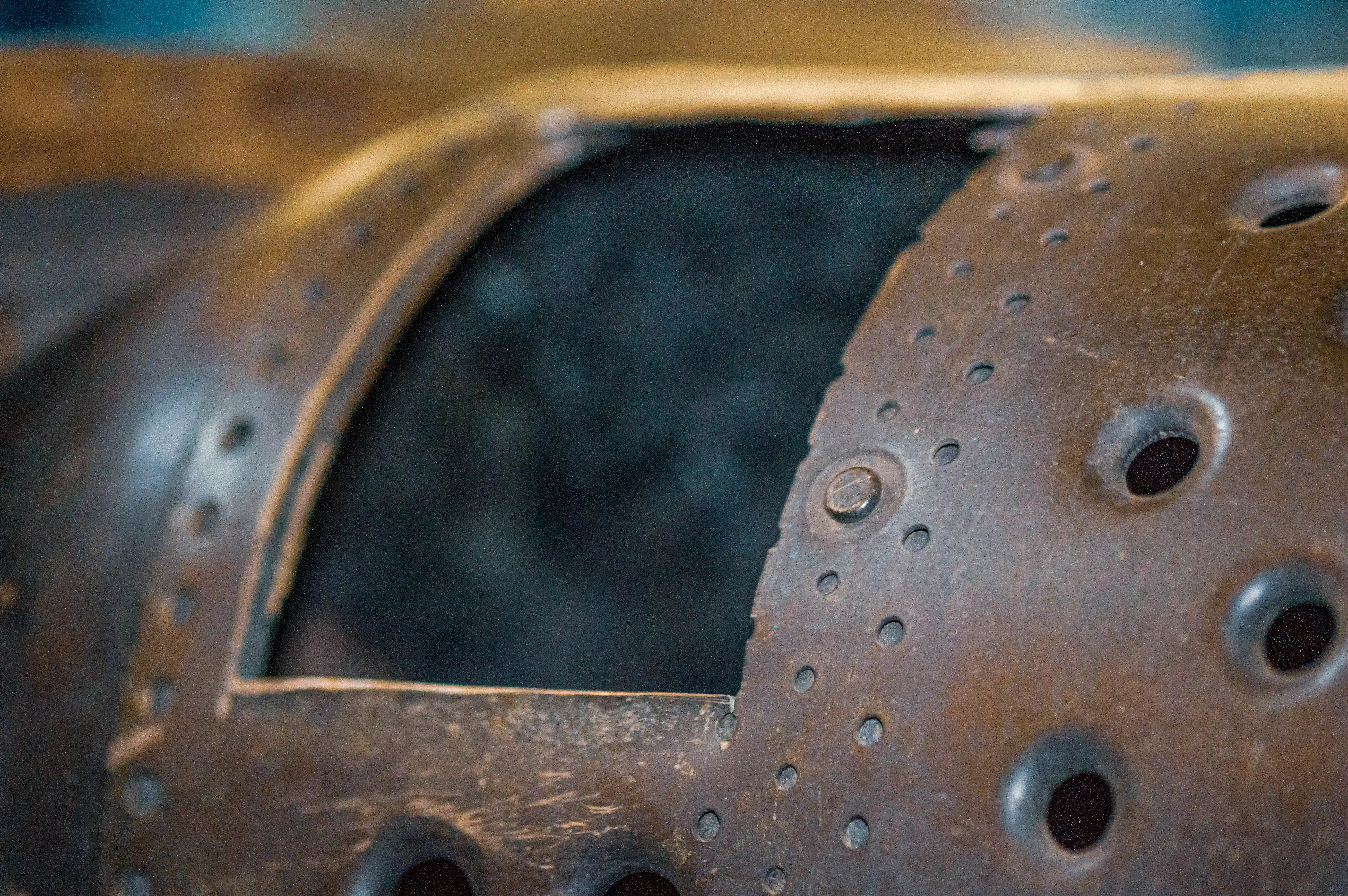 Extreme close-up of a pitted and riveted metal surface with a rectangular opening, showing signs of significant weathering and wear.