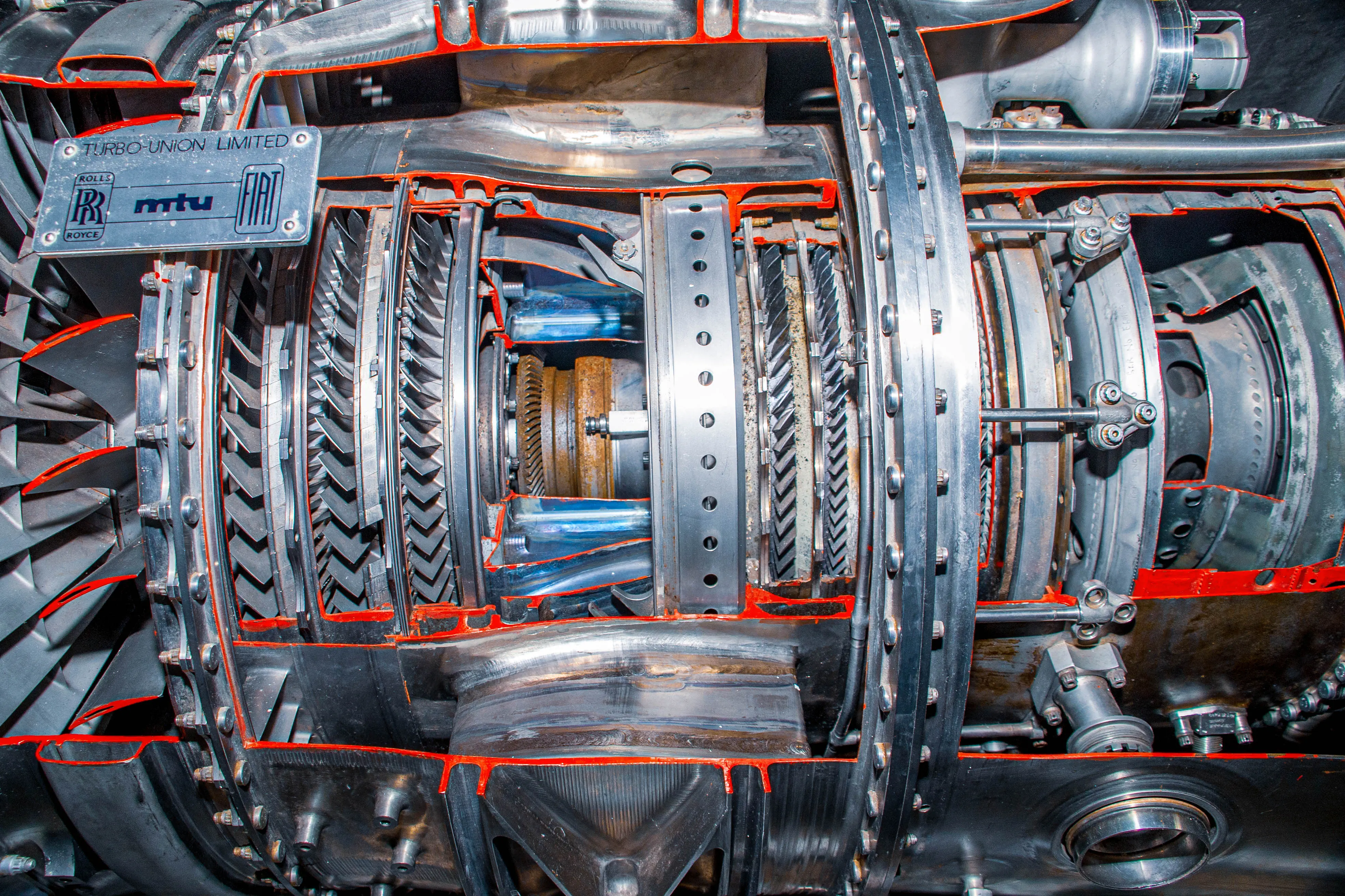 A cross-section of a powerful jet engine, revealing multiple stages of intricately designed turbine and compressor blades, along with gears and internal machinery, set against a dark background.