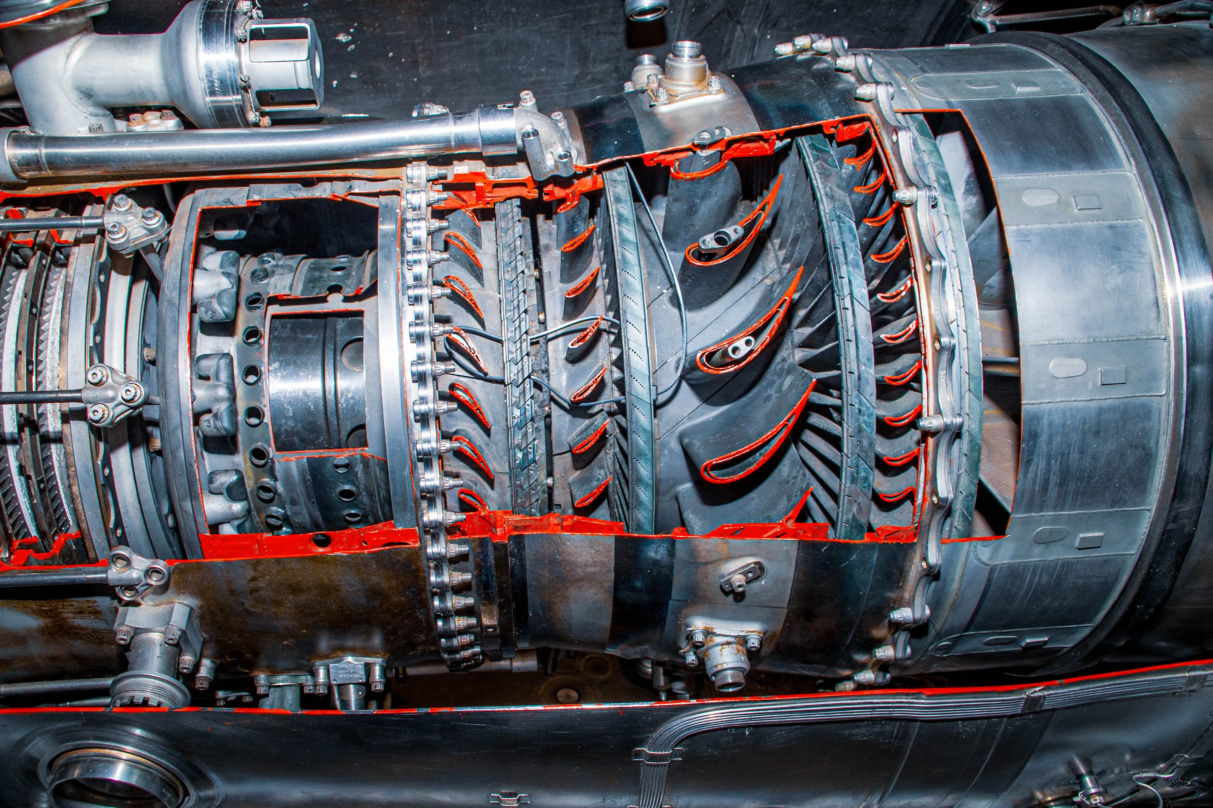 A cutaway section of a jet engine, showing multiple rows of fan blades and internal components with red accents.