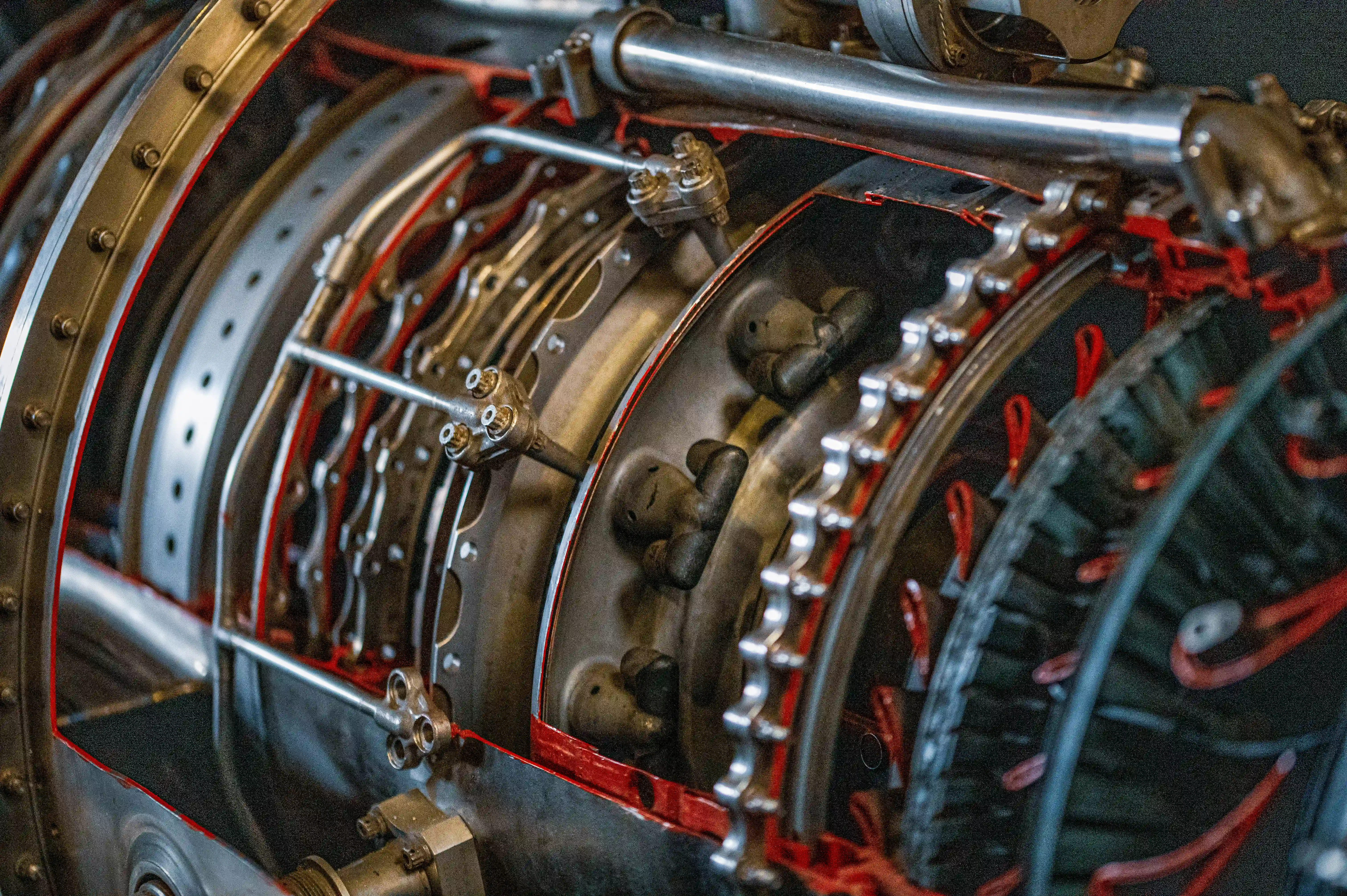A close-up photograph revealing the complex inner workings of a jet engine, with visible gears, pipes, and mechanical parts in metallic and red colours.