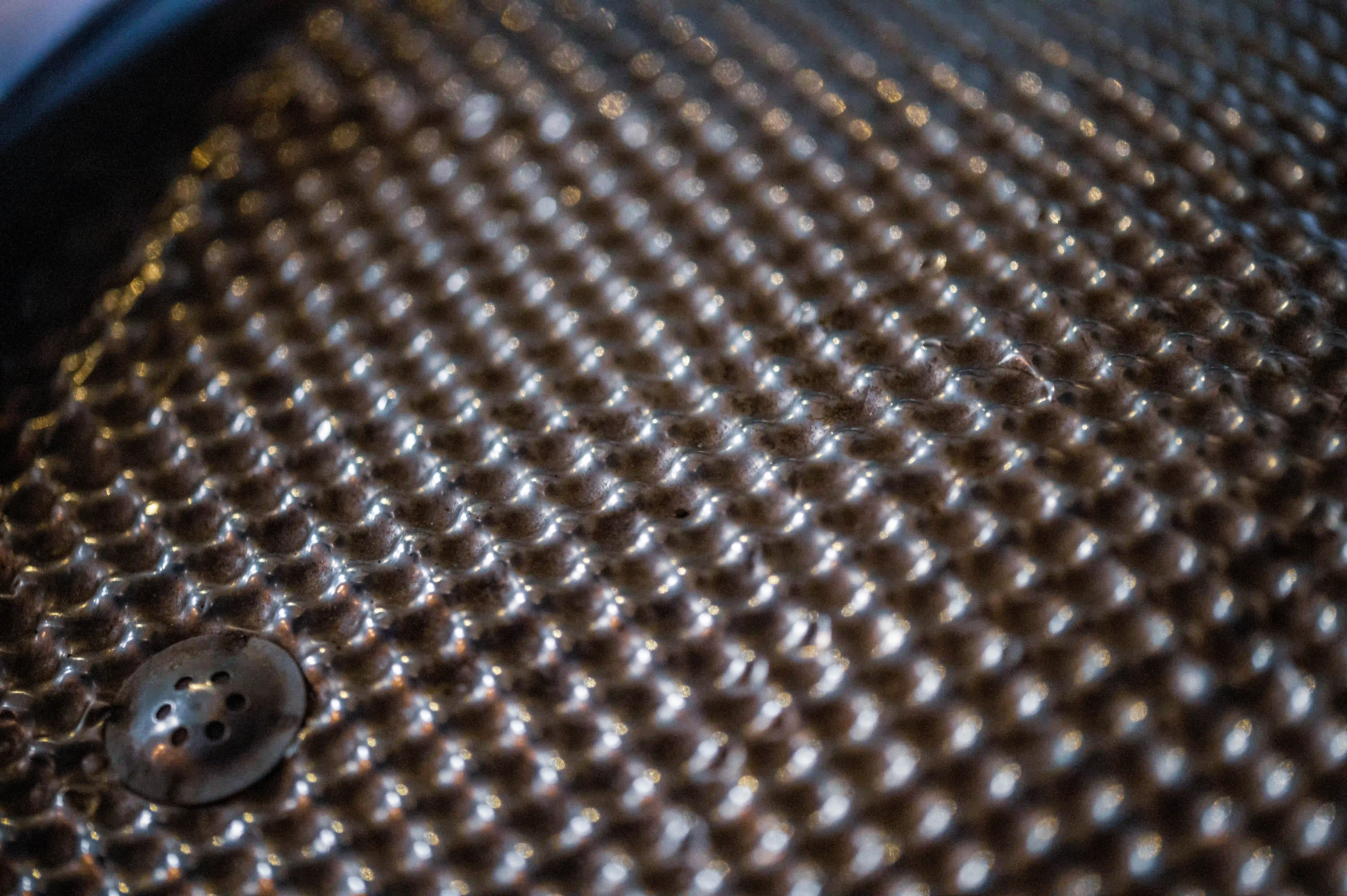 Close-up shot of a metal grater's surface, showing a regular pattern of raised bumps and a small drain hole.