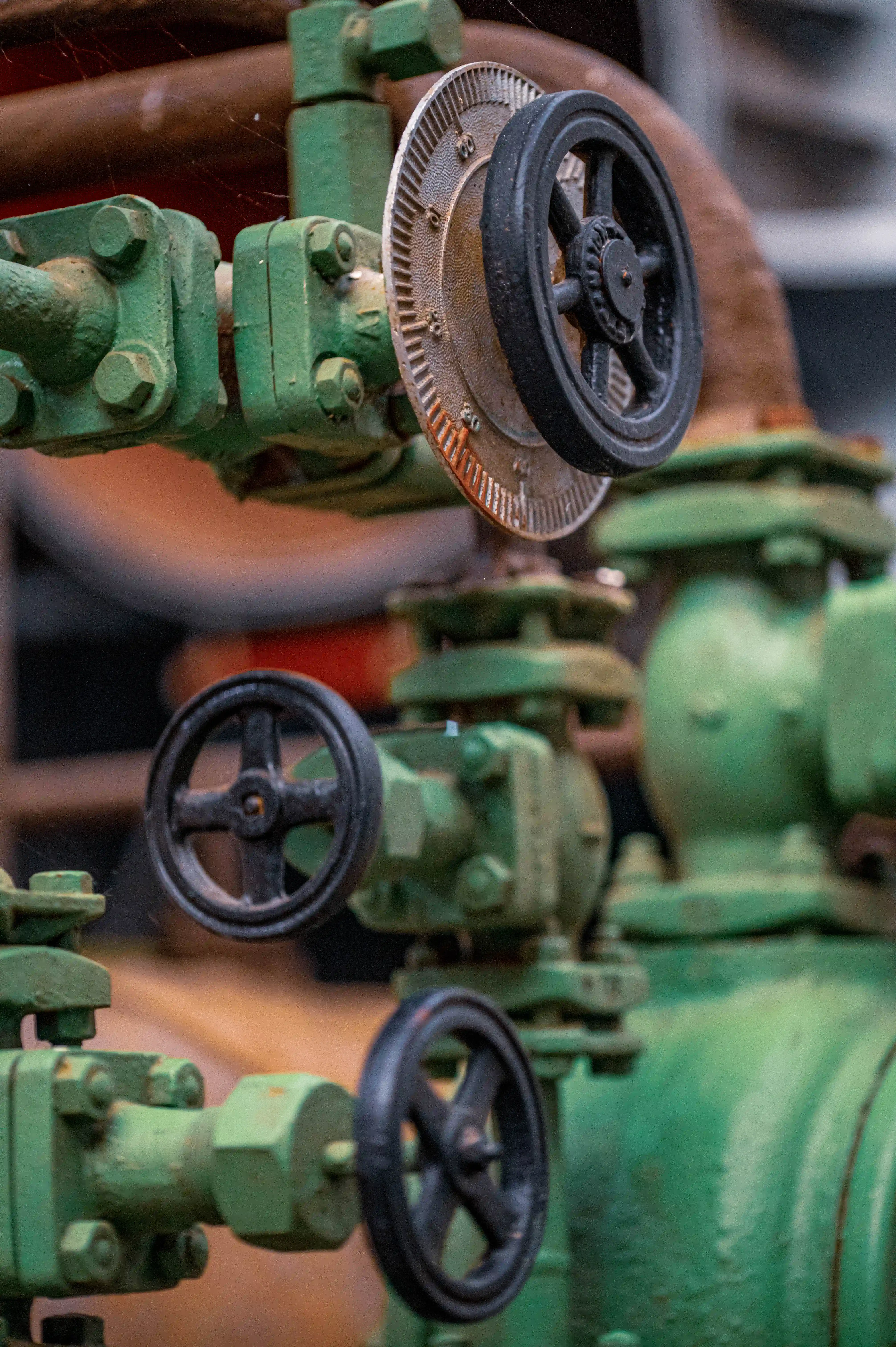 A detailed shot of industrial pipes and valves painted green, with several black handwheels used for operation.