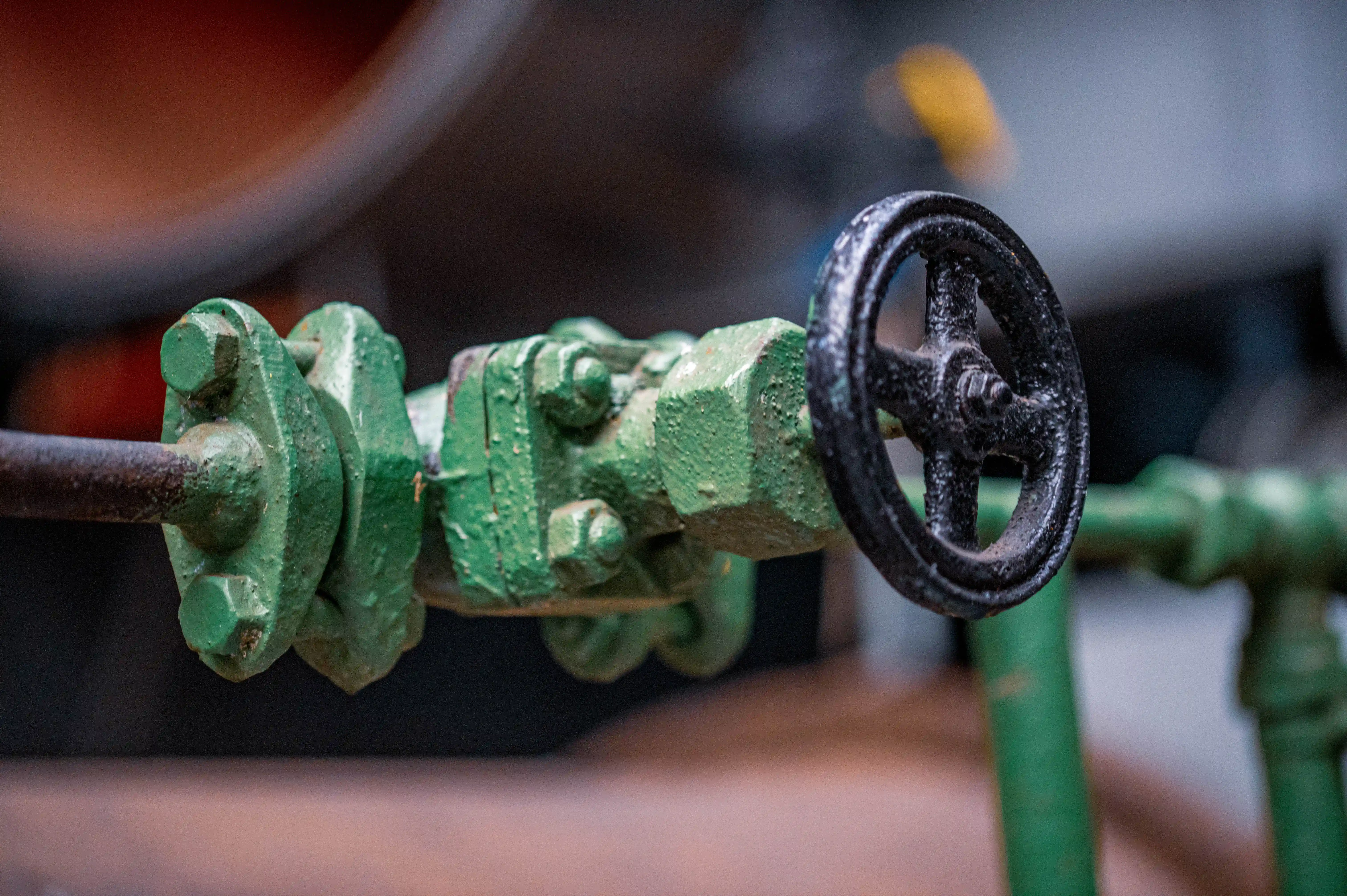 Close-up of a textured, green industrial valve with a black handwheel, set against a softly blurred background.