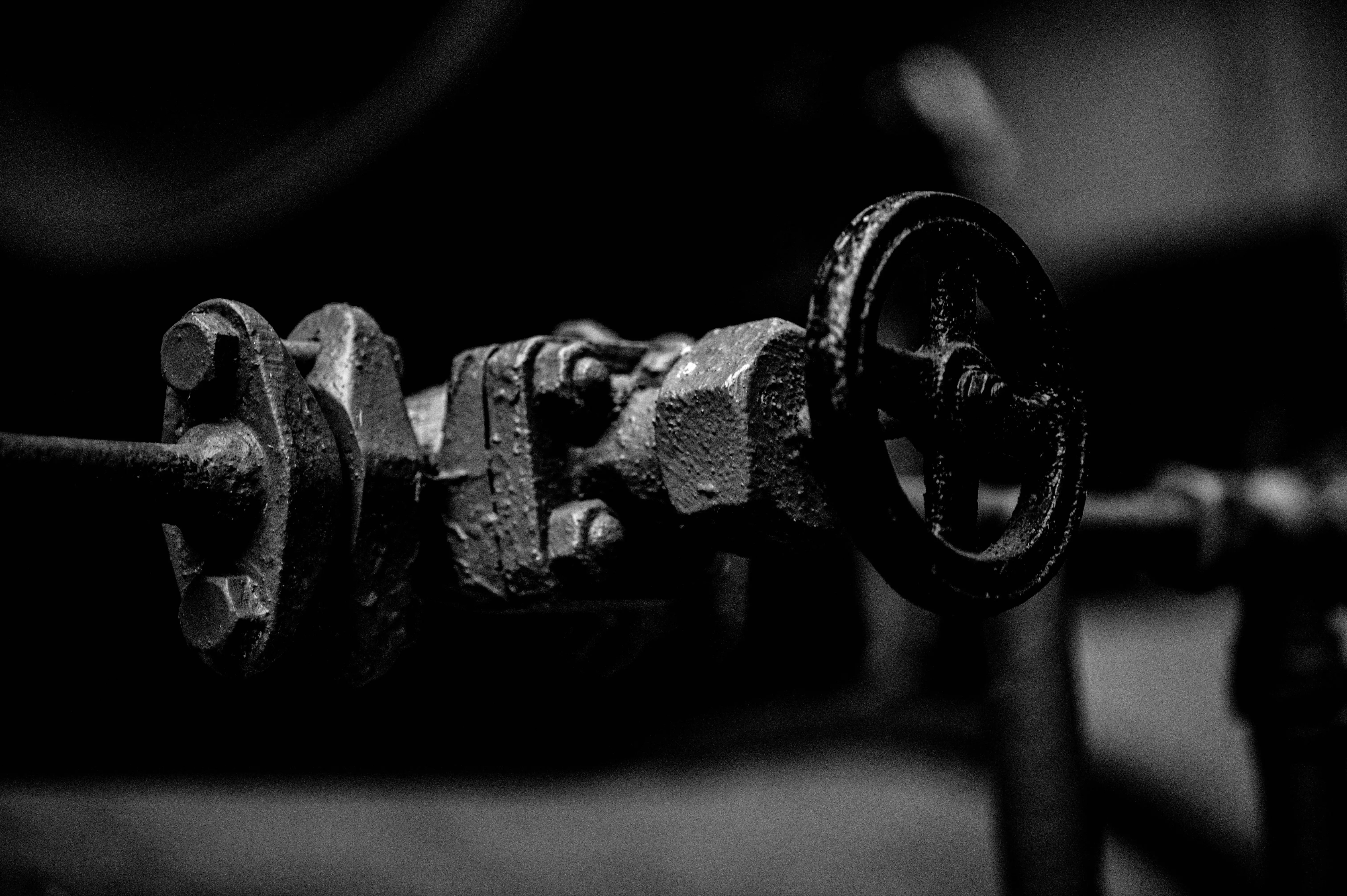 A monochrome close-up image of an industrial valve with a handwheel, showcasing its rough, metallic texture and bolted construction.