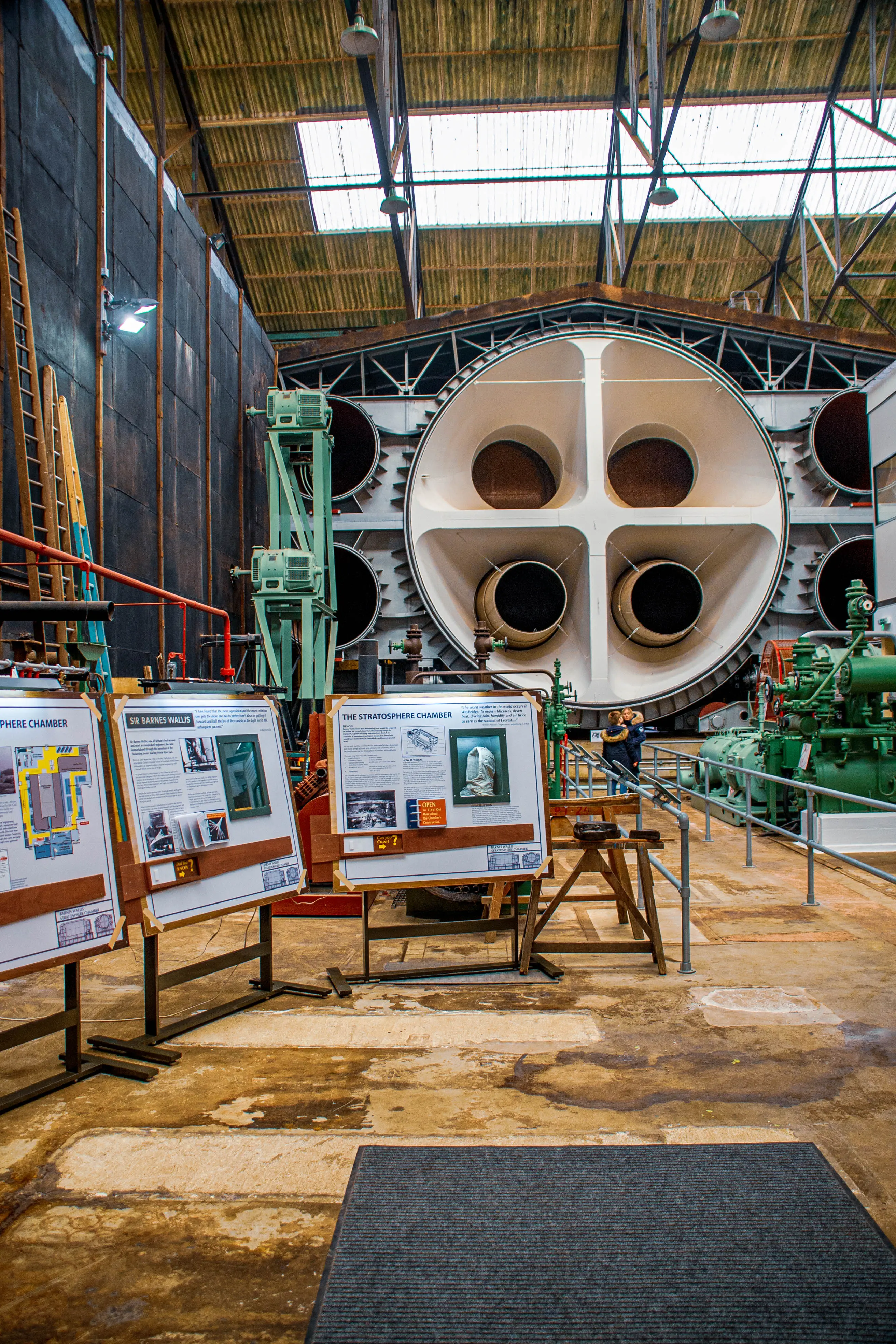 Display boards detailing the Stratosphere Chamber and Sir Barnes Wallis are positioned in front of a large, round, industrial engineering structure with multiple large openings.