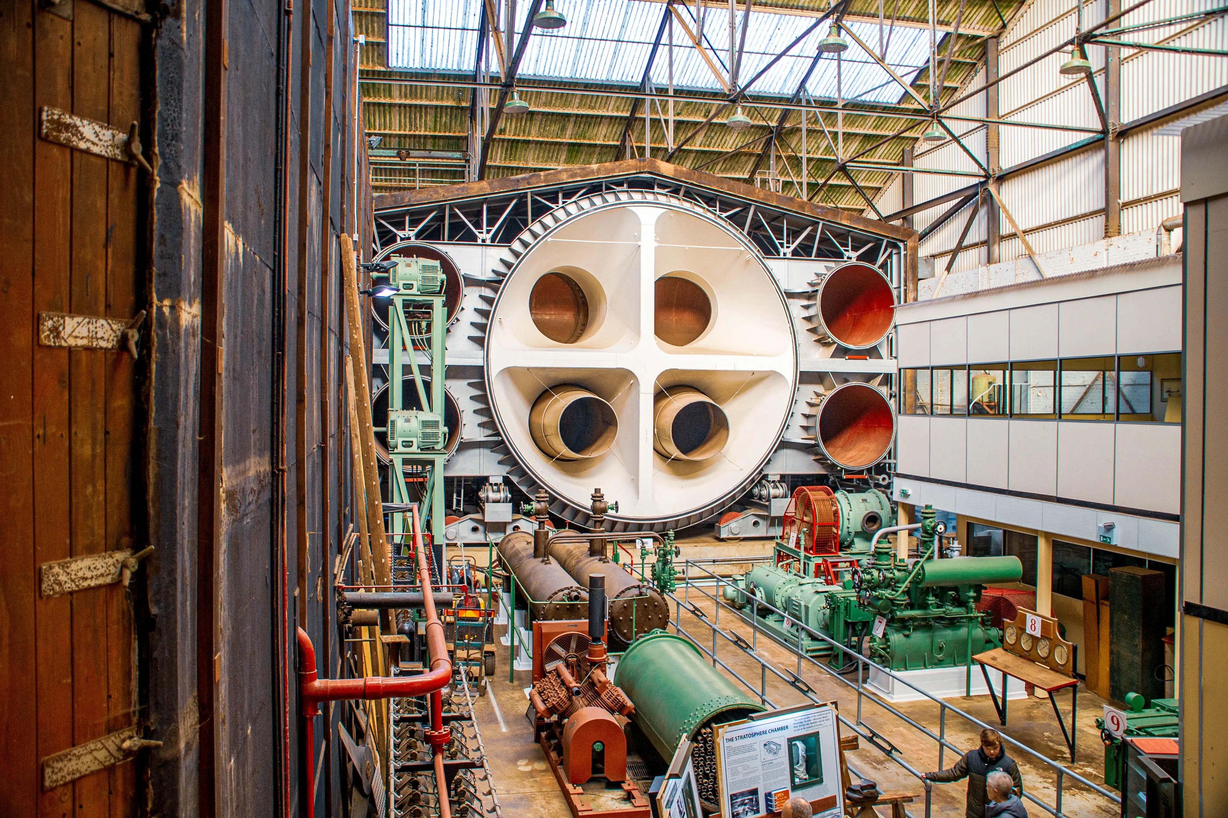 Interior view of a museum showcasing a large, circular scientific apparatus with multiple openings, surrounded by industrial machinery and equipment.