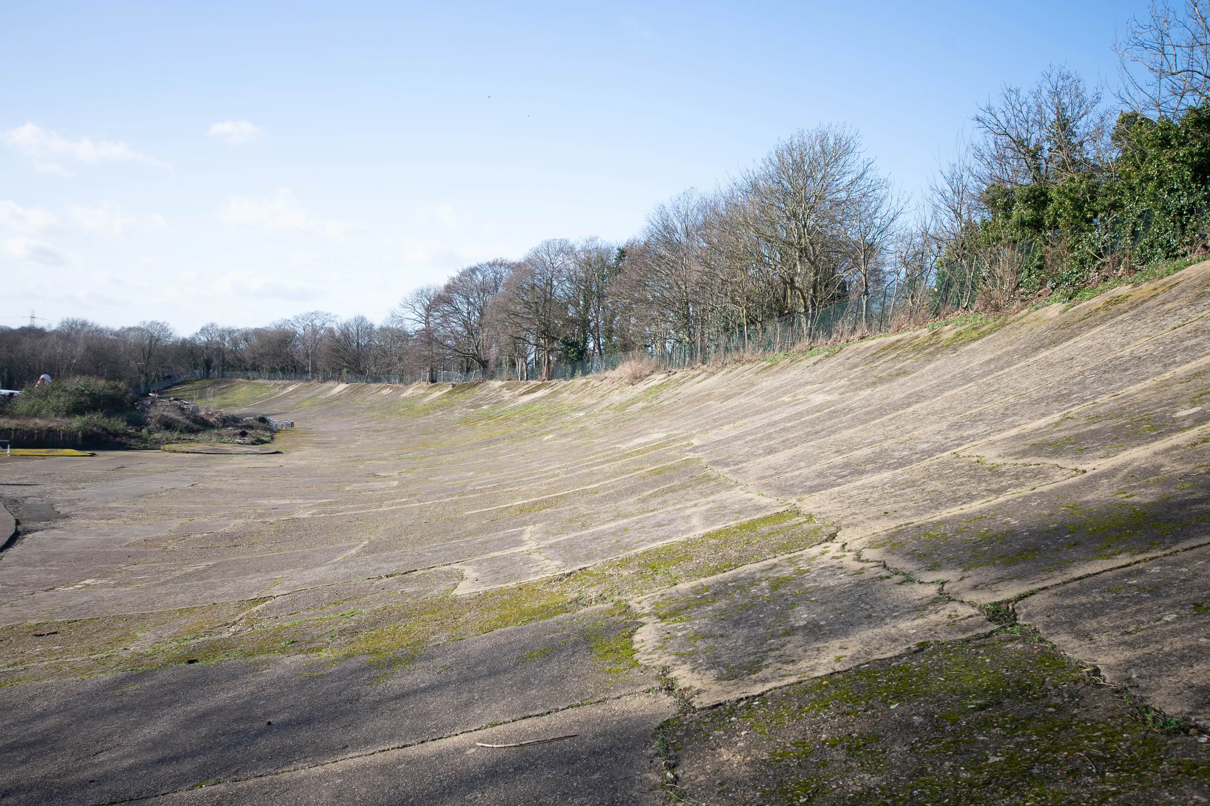A wide-angle view of the steep, concrete banking of the historic Brooklands race track, with trees and a blue sky overhead.