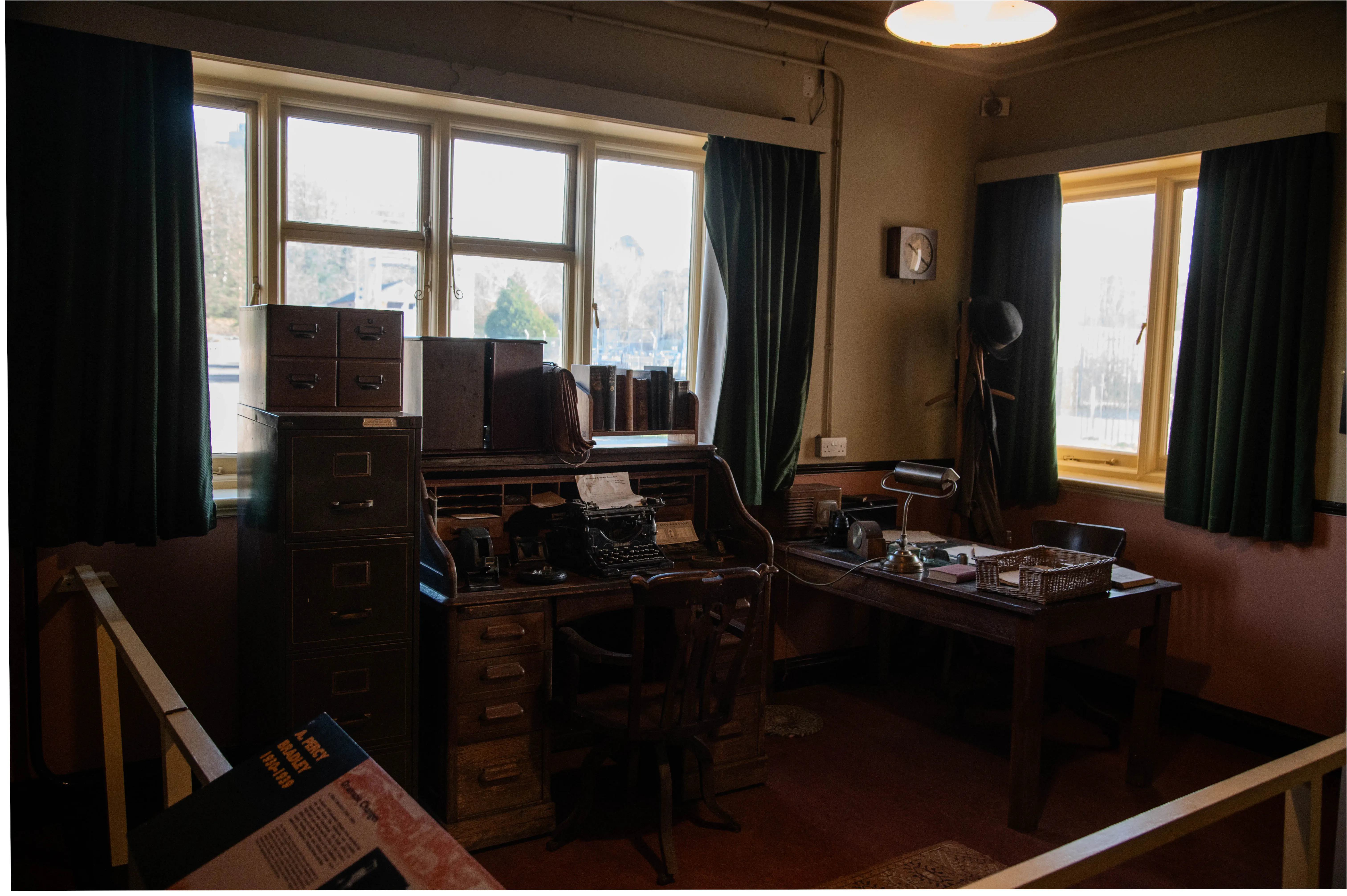 Interior view of a vintage office with a roll-top desk, typewriter, filing cabinets, and wooden furniture.