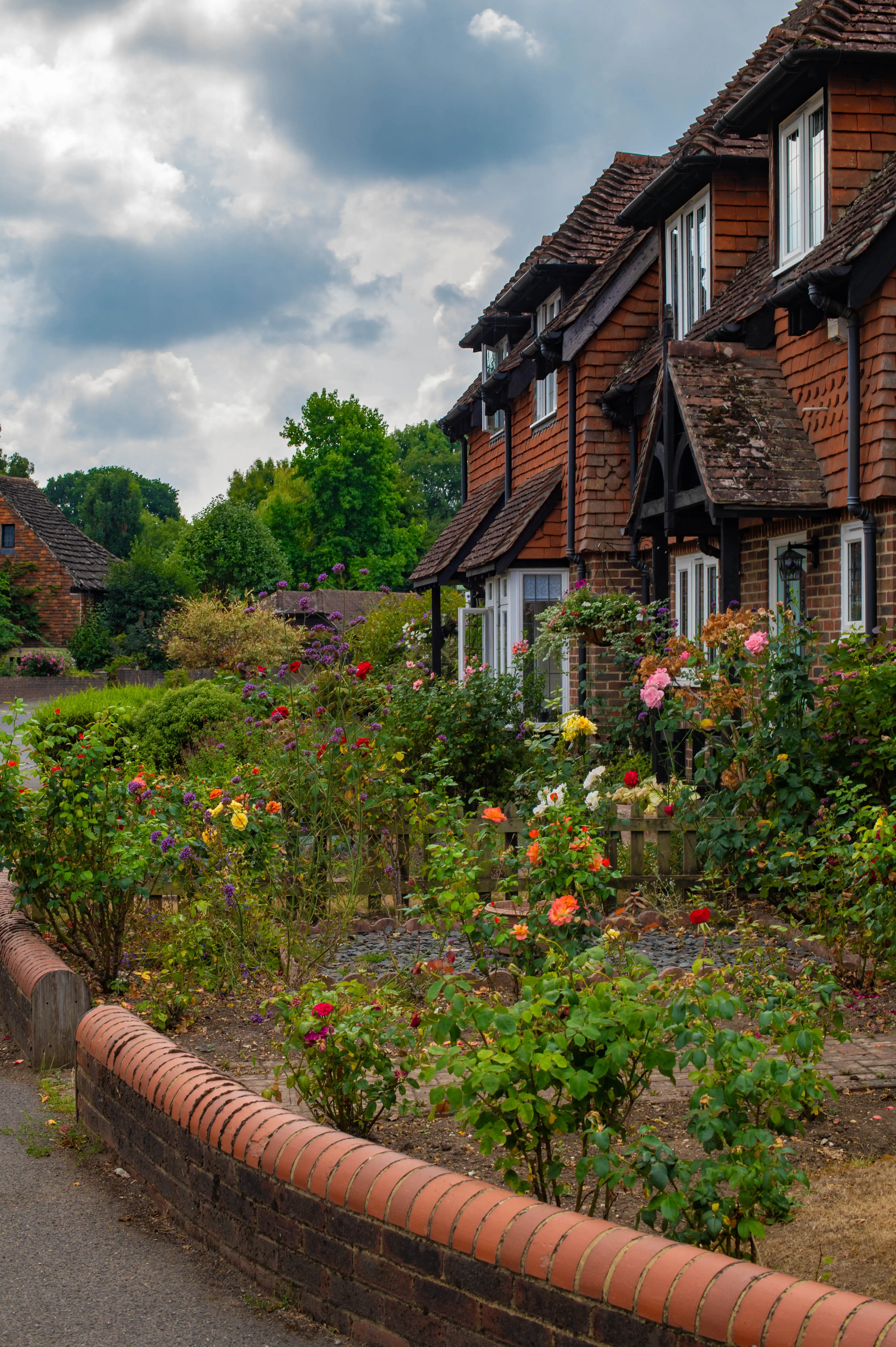 Brick house with steep roof, white windows and vibrant rose garden bordered by a curved brick wall.