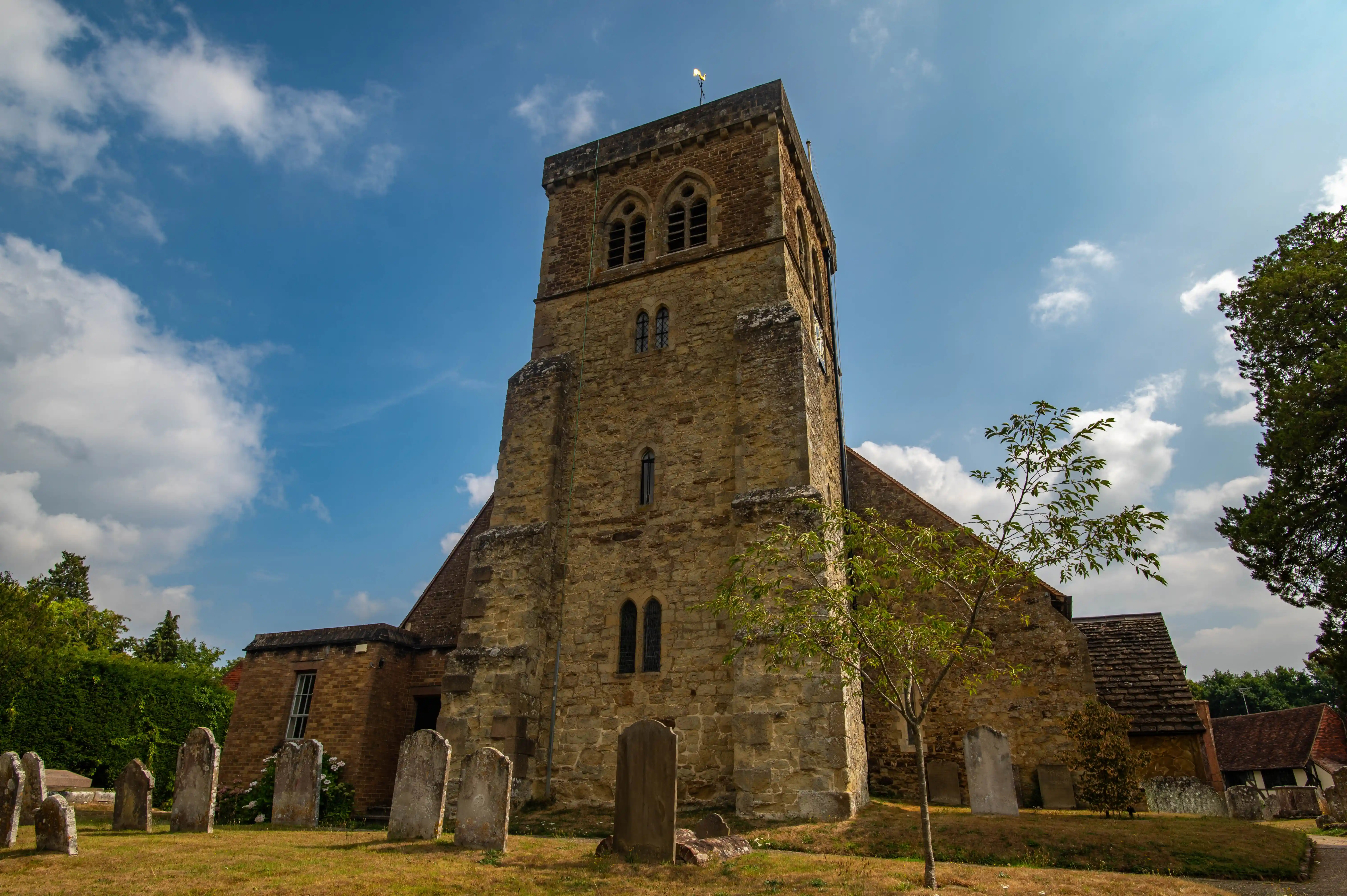 Stone church with square tower, arched windows and old gravestones in a rural English churchyard.