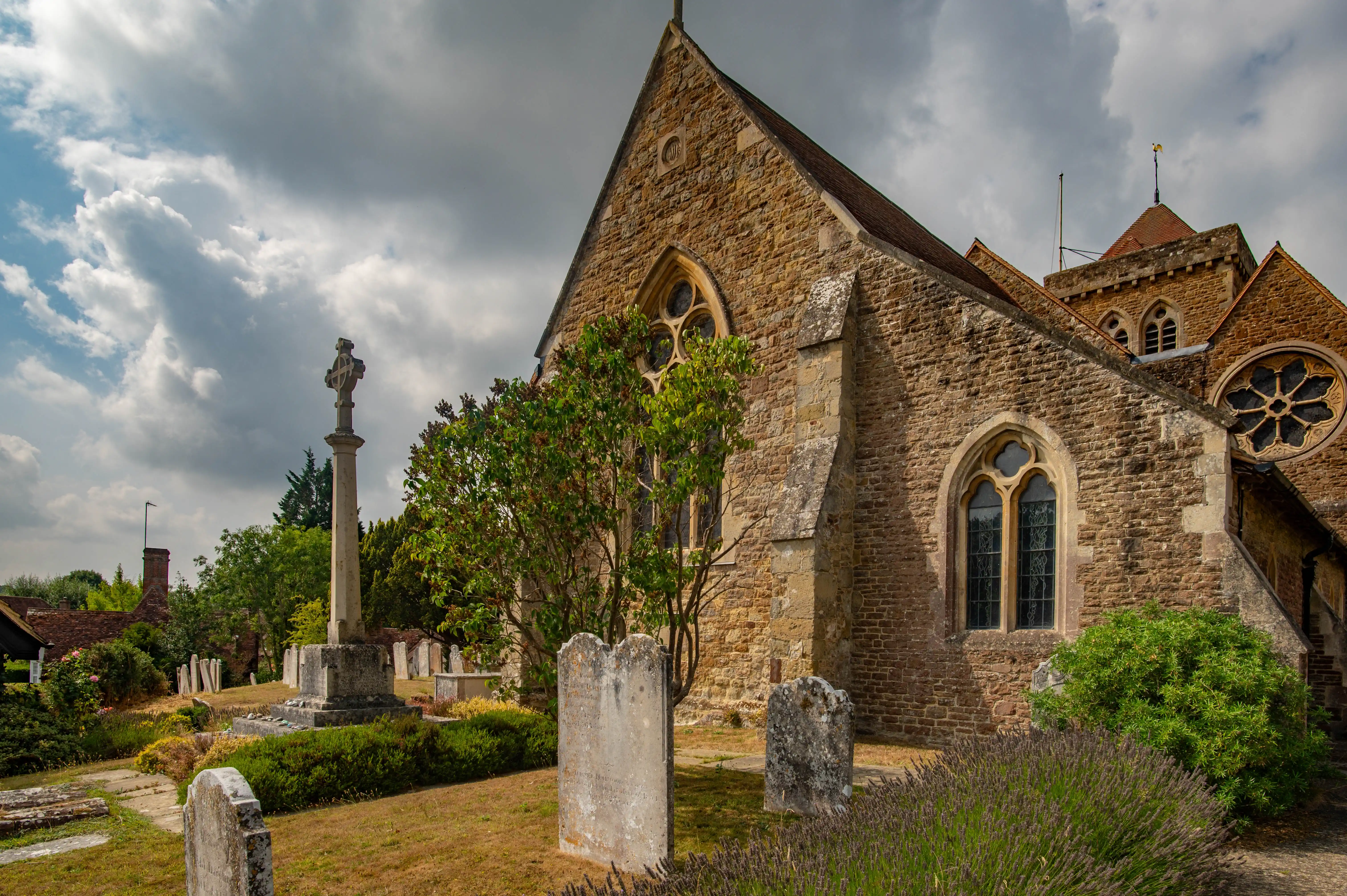 Gothic stone church with rose window, pointed-arch windows, tall cross monument and weathered headstones.