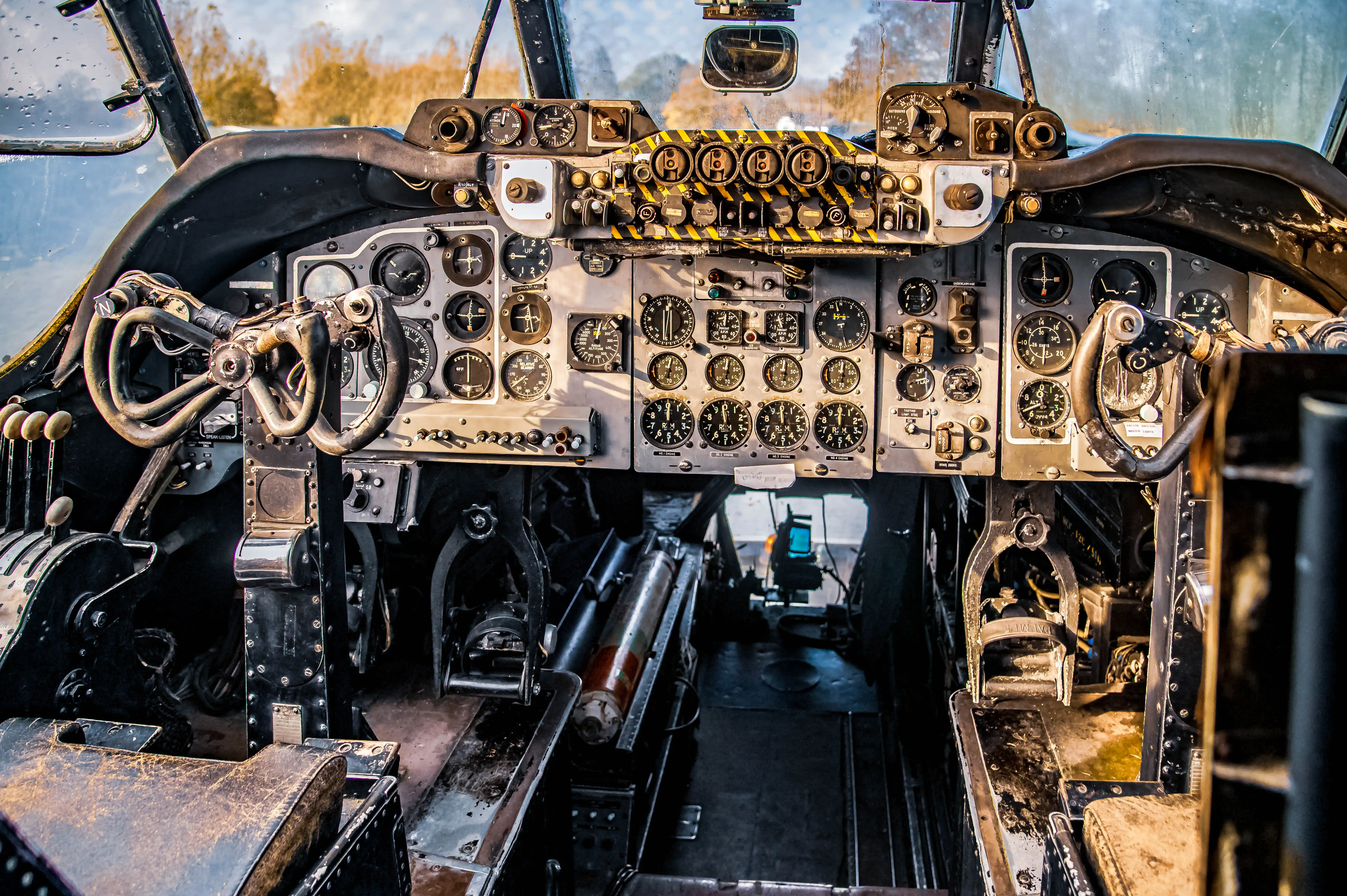 Interior view of a vintage aircraft cockpit, displaying a multitude of analogue gauges, dials, and two control yokes, with worn leather seats visible in the foreground.